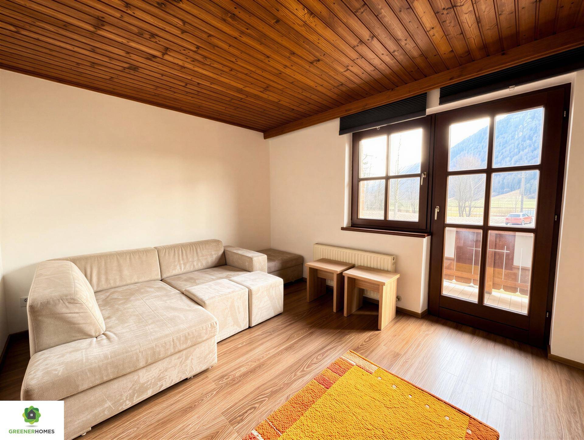 Gemütliches Wohnzimmer mit beigem Sofa, Holzbalkendecke und Blick auf die Berge.