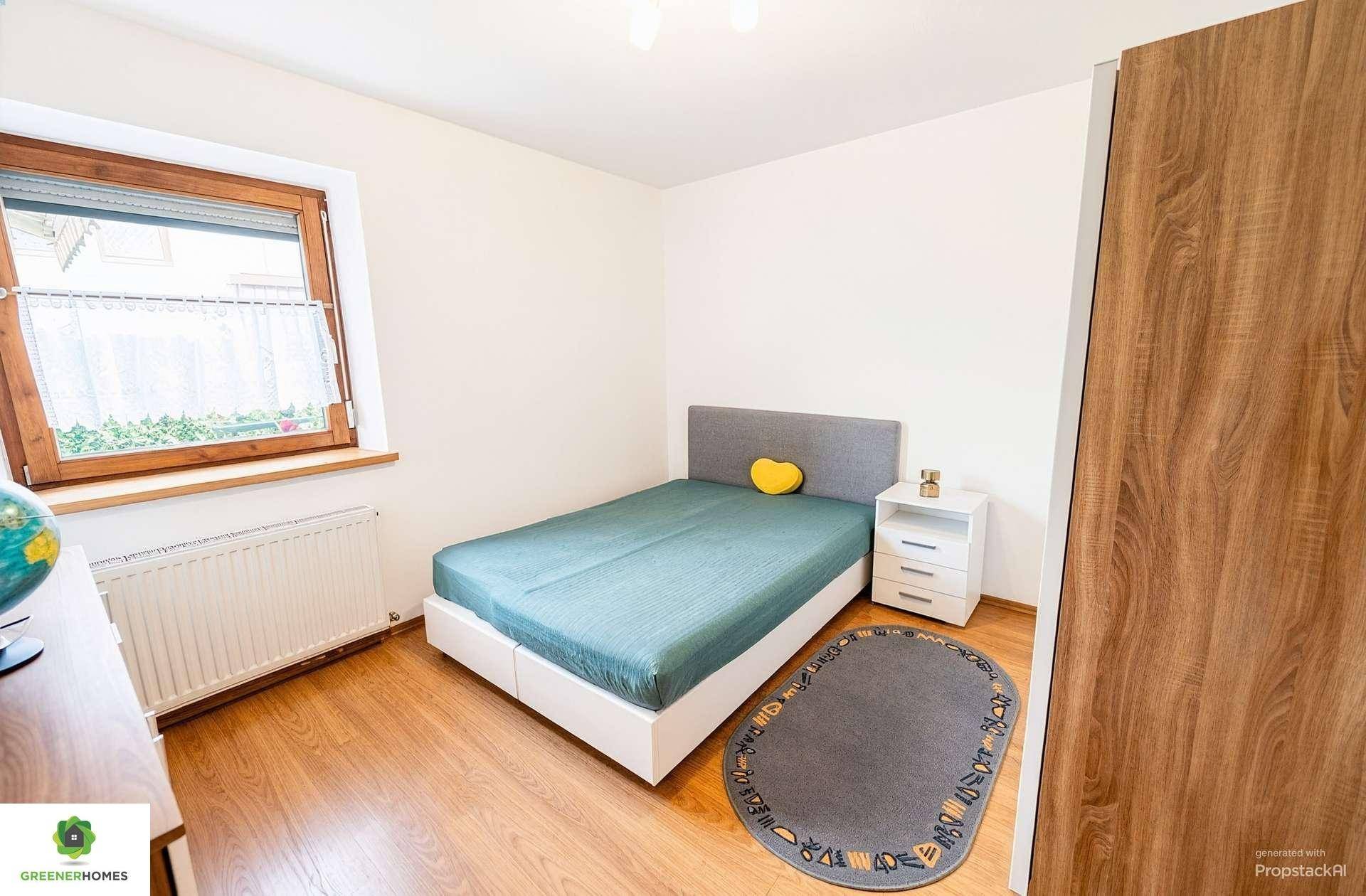 Schlafzimmer mit Holzboden, weißem Nachttisch und blaugrüner Tagesdecke.