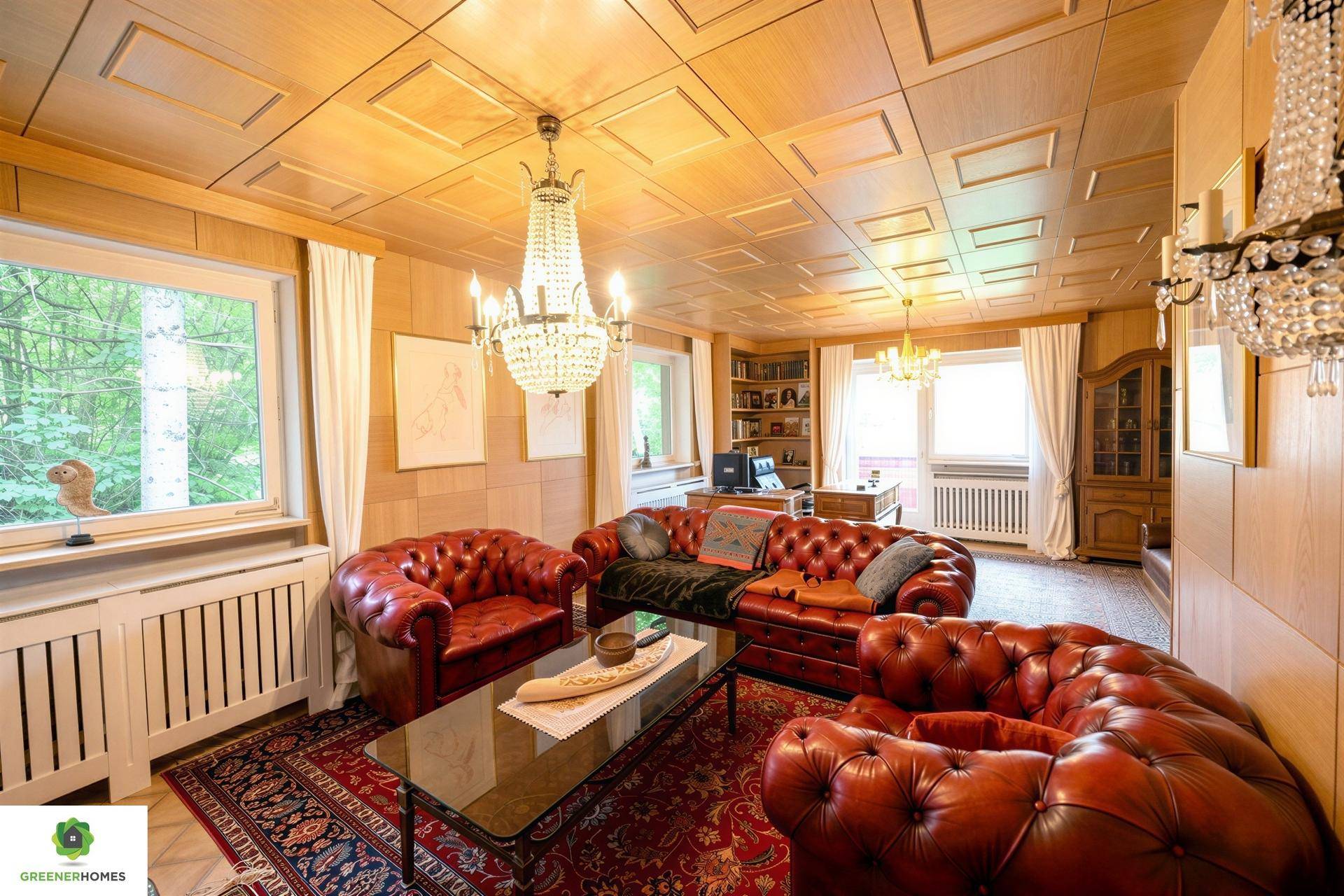 Elegantes Wohnzimmer mit roten Ledersofas, Holzdecke und großen Fenstern mit Waldblick.