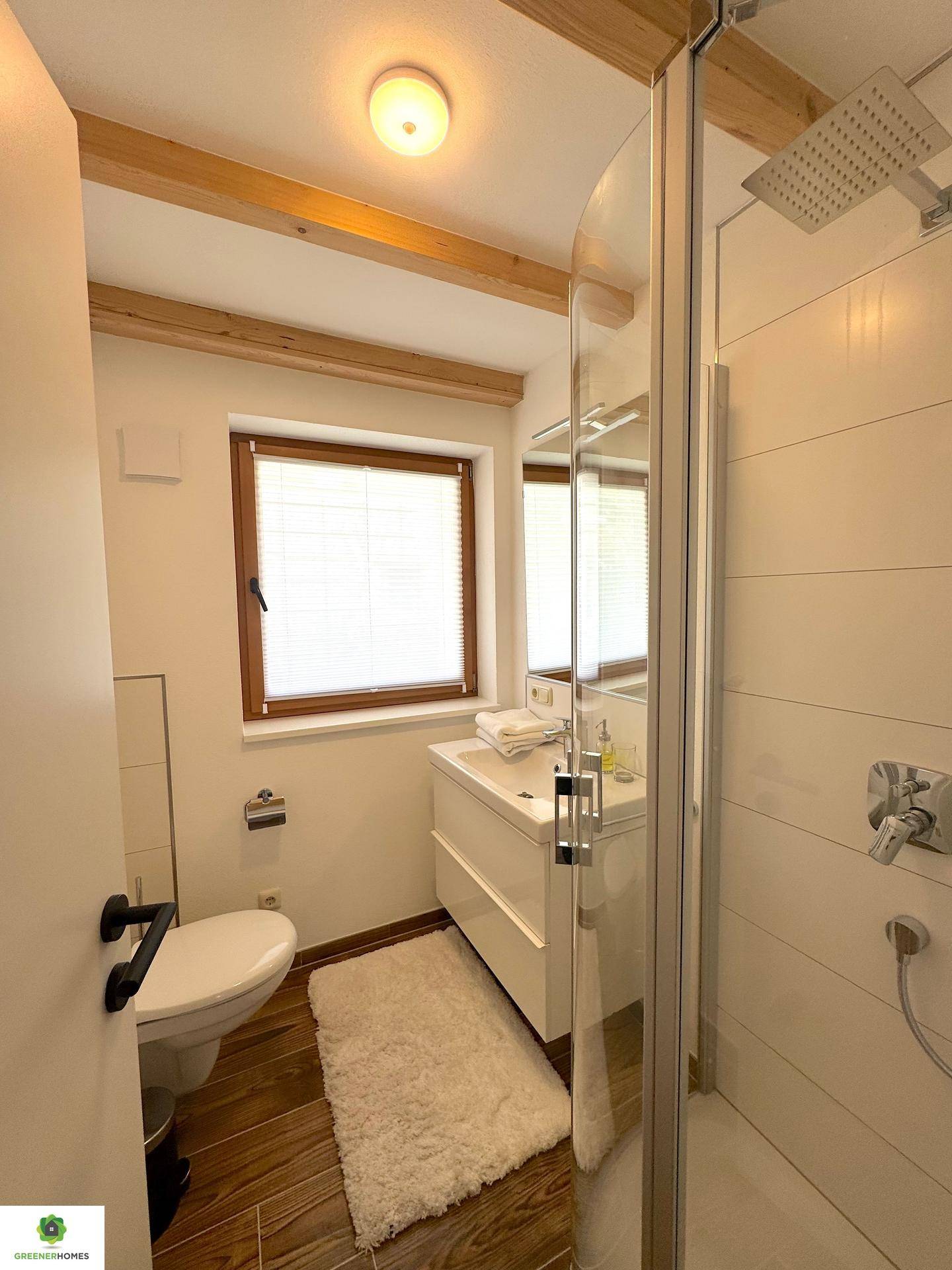Kleines, helles Badezimmer mit Dusche, WC, Waschtisch und Fenster für Tageslicht.