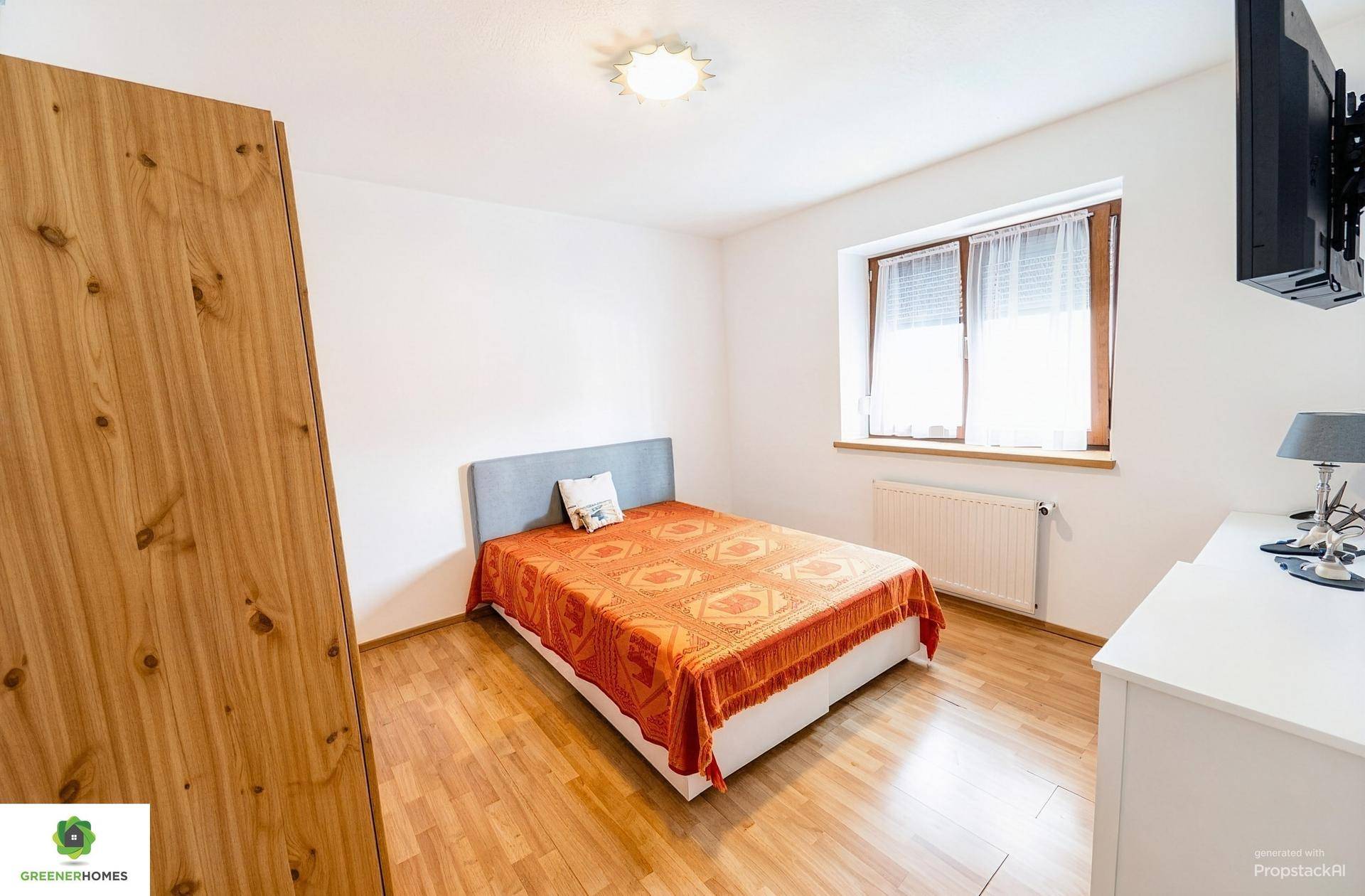 Schlafzimmer mit Holzboden, weißer Einrichtung und orangefarbener Tagesdecke.