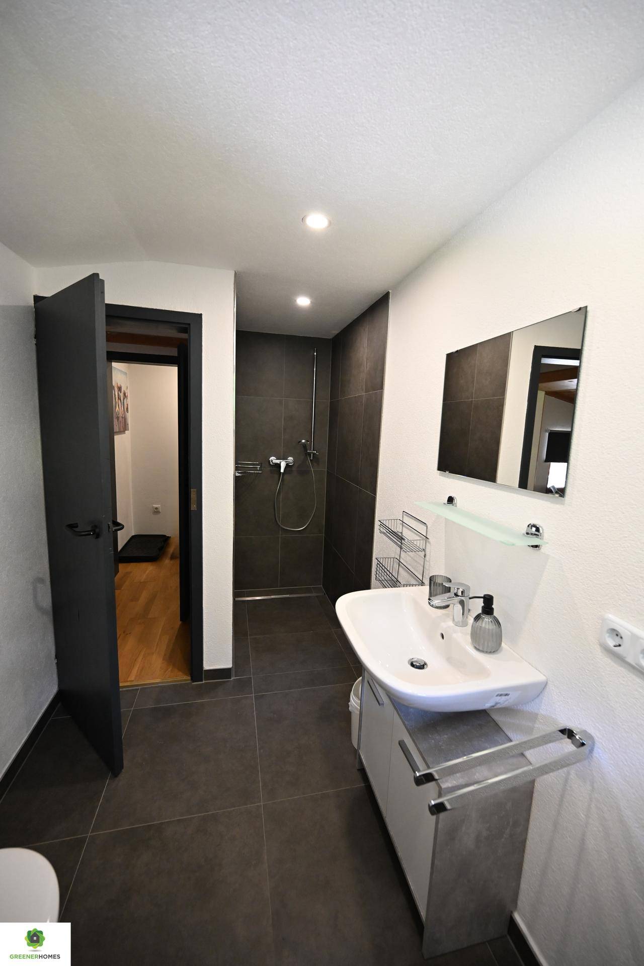 Modernes Badezimmer mit dunklen Fliesen, Waschbecken und einer geräumigen Dusche.