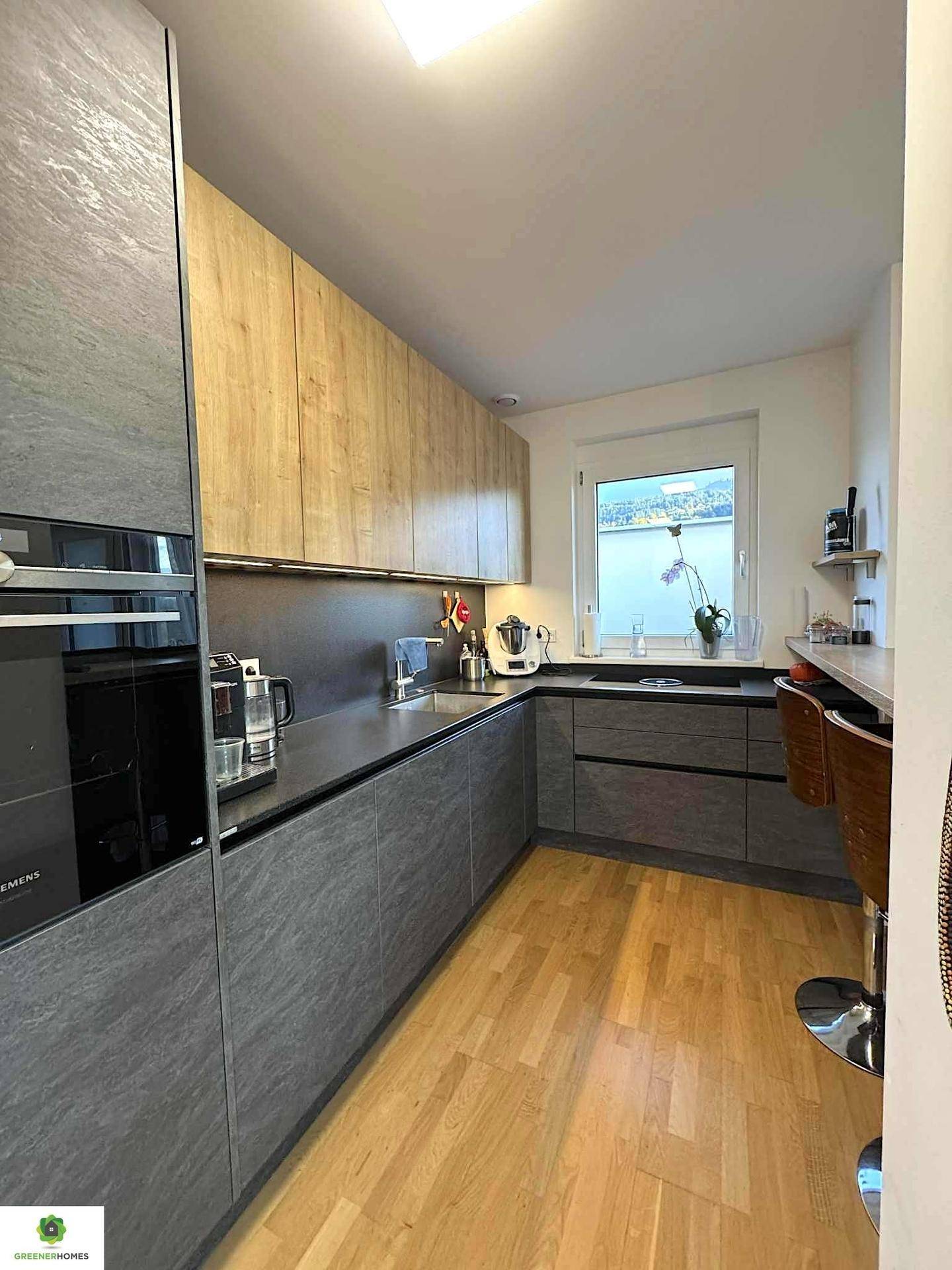 Moderne Küche mit grauen und holzfarbenen Schränken, integrierten Geräten und Seeblick.