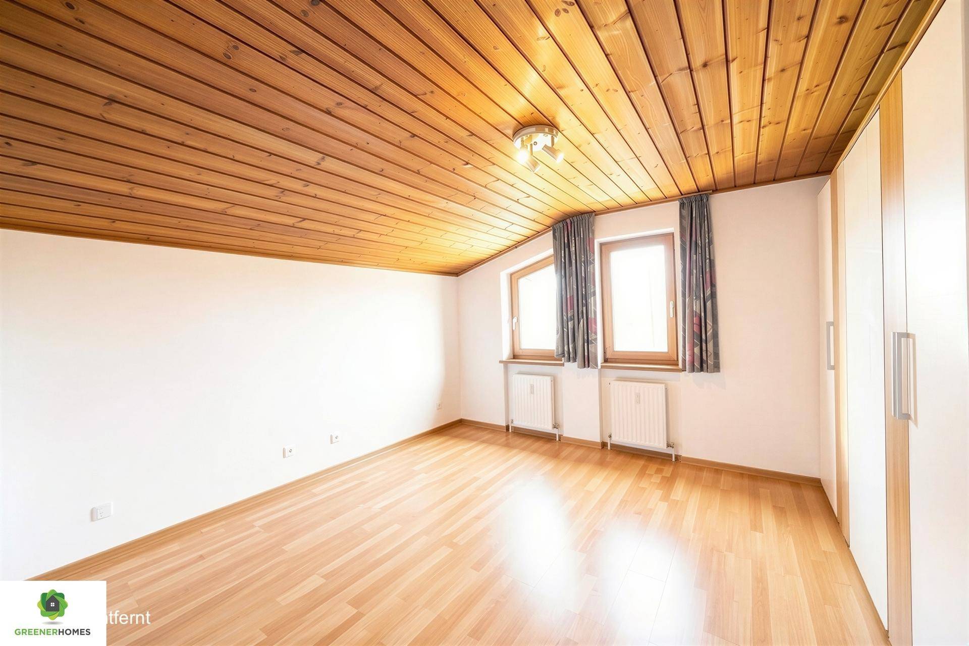 Schlafzimmer mit Holzboden, Holzdecke und zwei Fenstern für natürliches Licht.