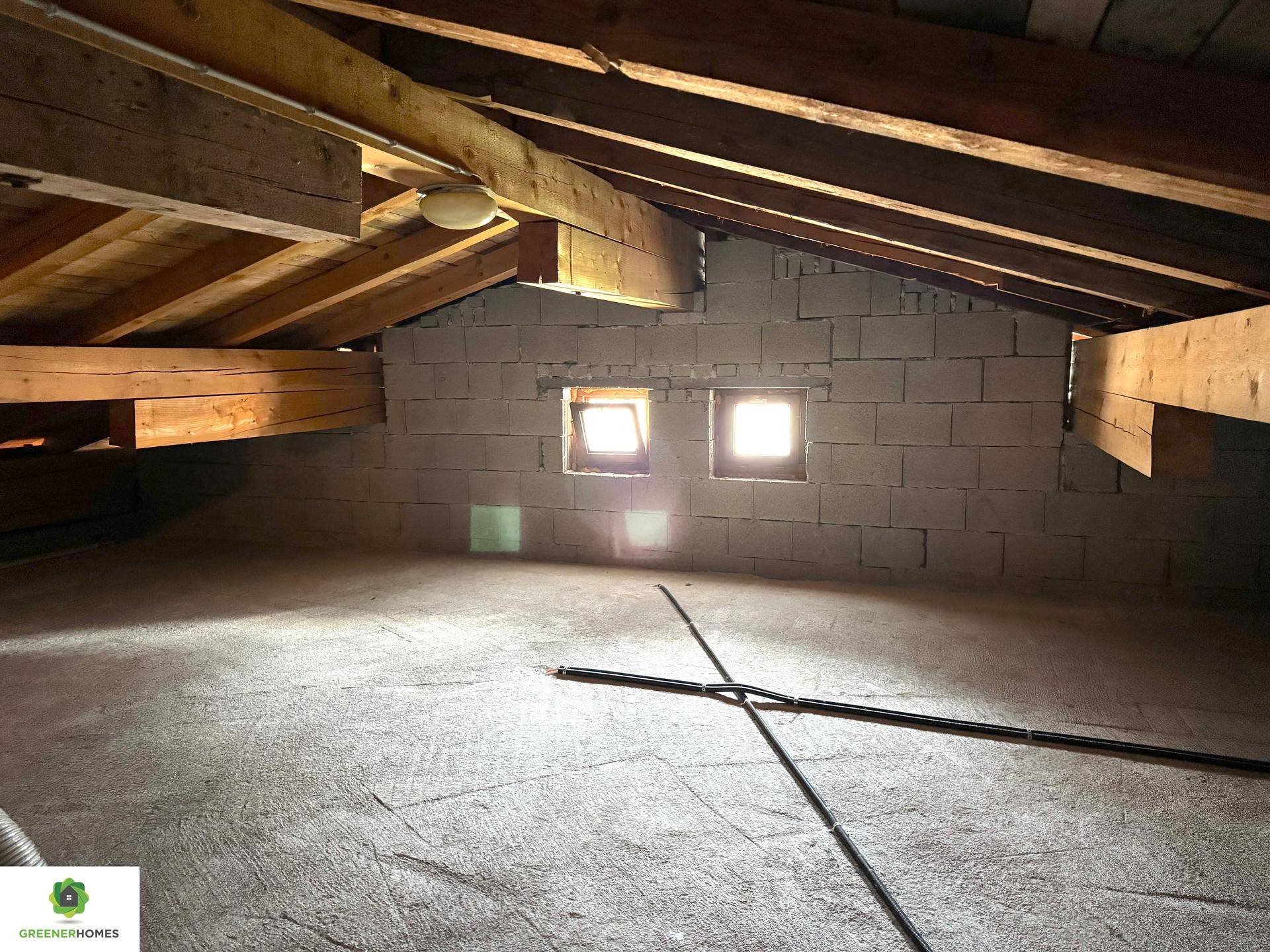 Unausgebauter Dachboden mit sichtbaren Holzbalken und kleinen Fenstern, bietet Ausbaupotenzial.