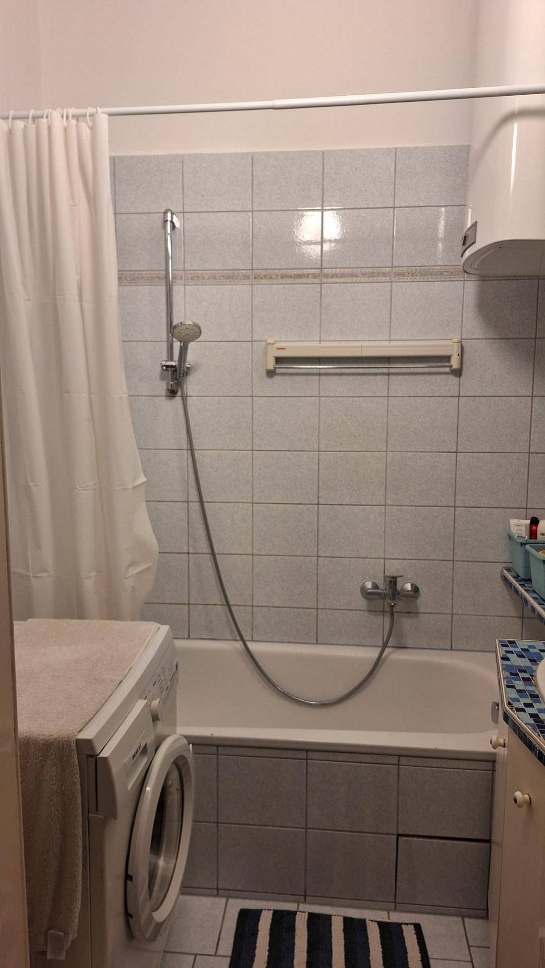 Badezimmer mit Badewanne, Duschvorhang und hellen Fliesen an den Wänden.