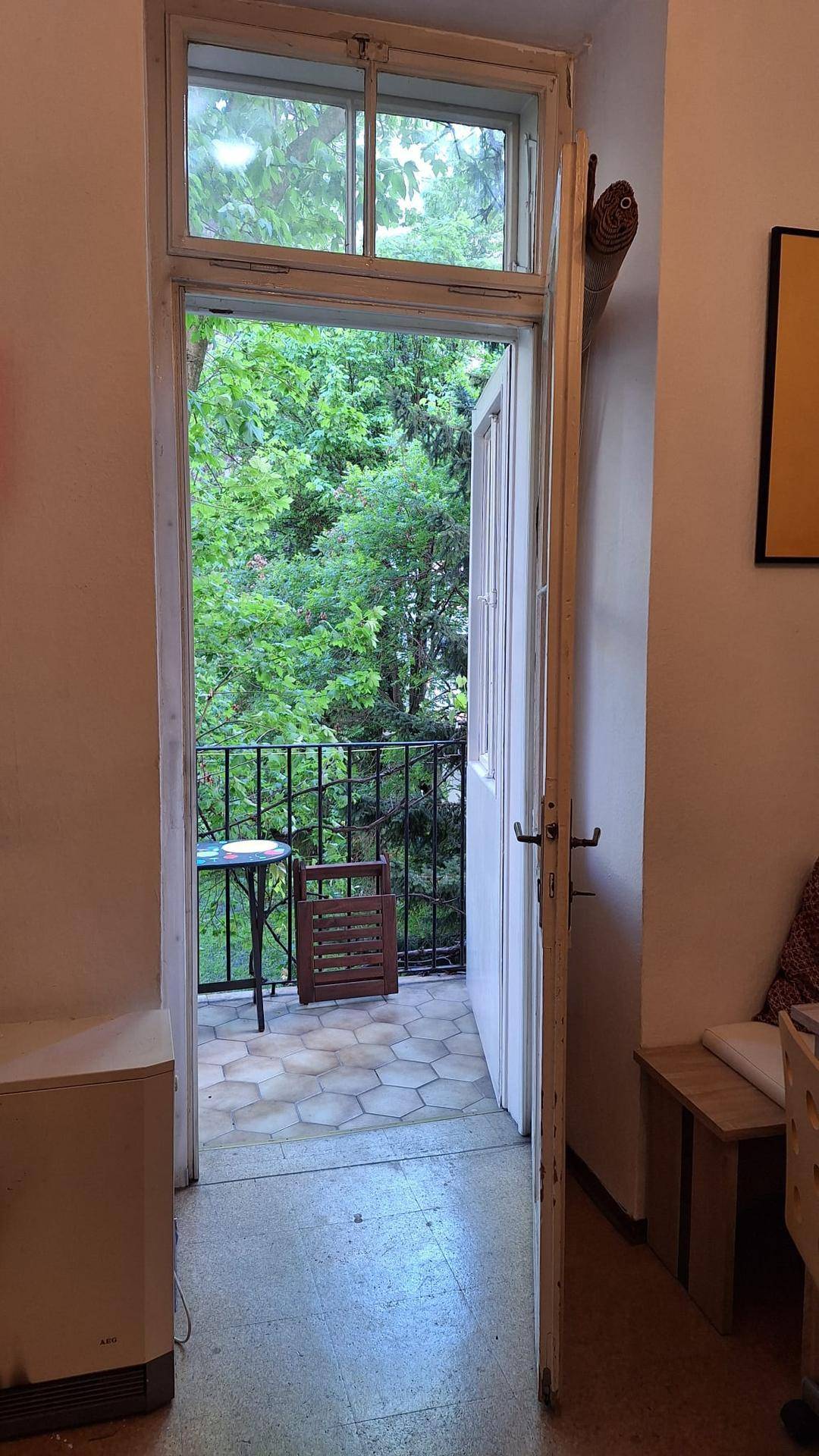 Offene Tür führt zu einem kleinen Balkon mit Tisch, Stühlen und Blick ins Grüne.