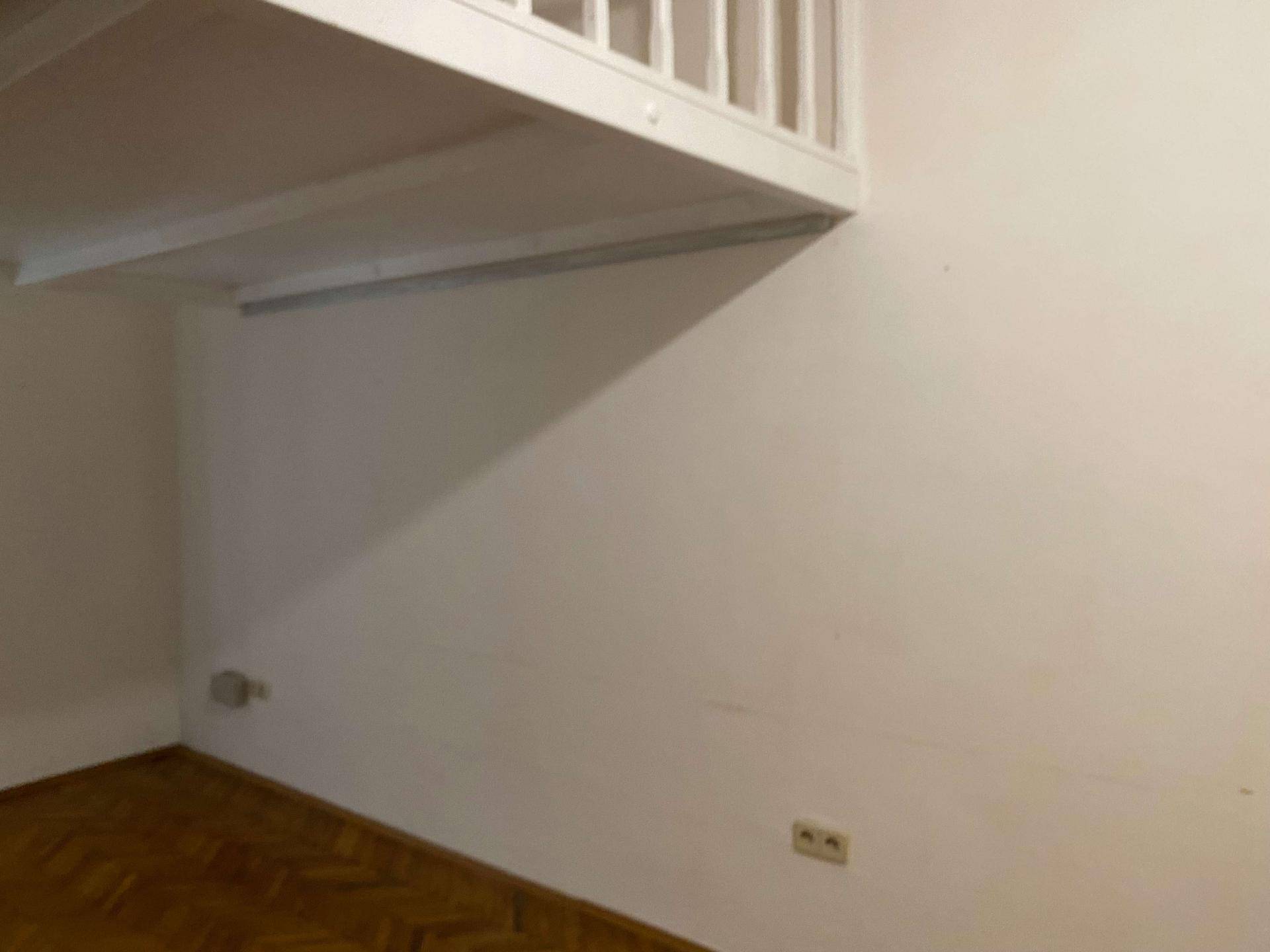 Leere Ecke eines Zimmers mit weißen Wänden und Fischgrätparkett unter einer Hochbett-Konstruktion.