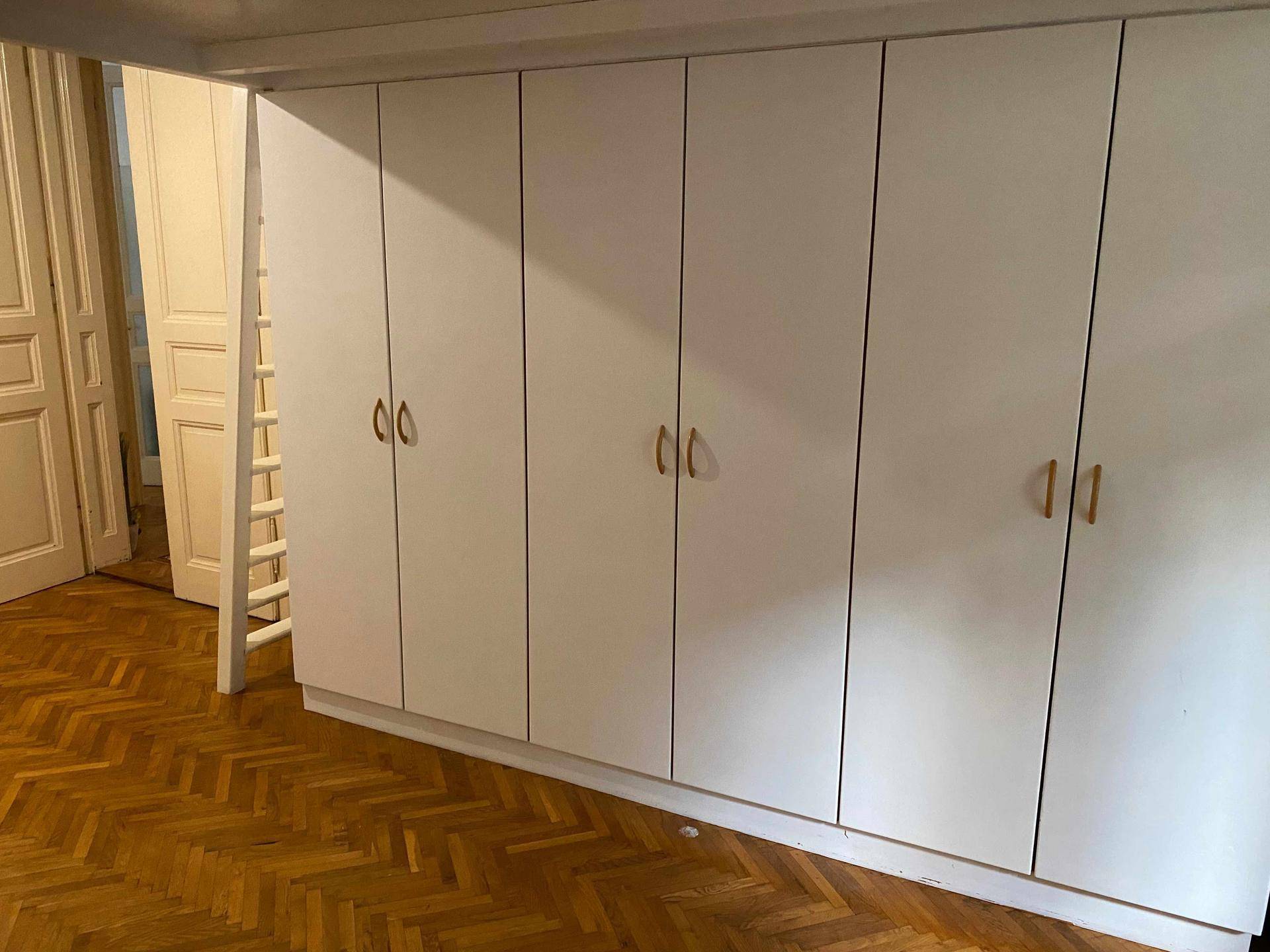 Weiße Einbauschränke in einem Zimmer mit Fischgrätparkett und Zugang zu einem Hochbett.