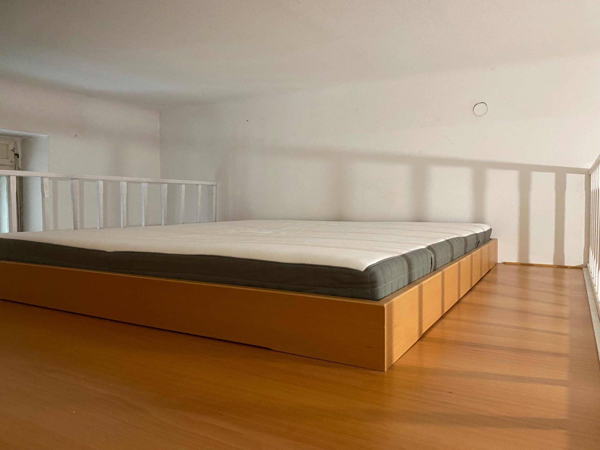 Schlafbereich auf einer Hochbett-Ebene mit Matratze, Holzfußboden und weißem Geländer.