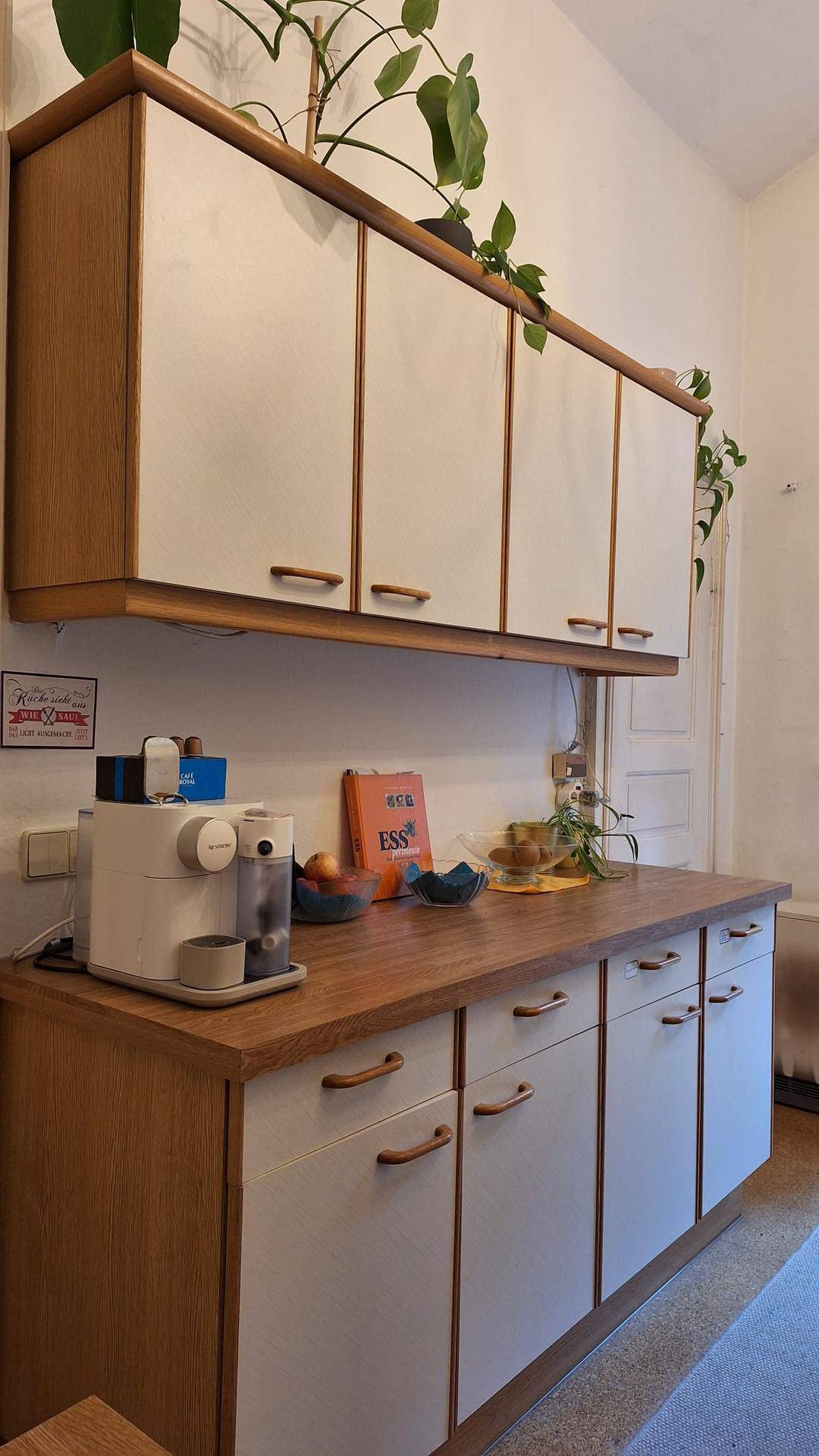 Küchenzeile mit Holz-Arbeitsplatte, weißen Hängeschränken und einer Kaffeemaschine.