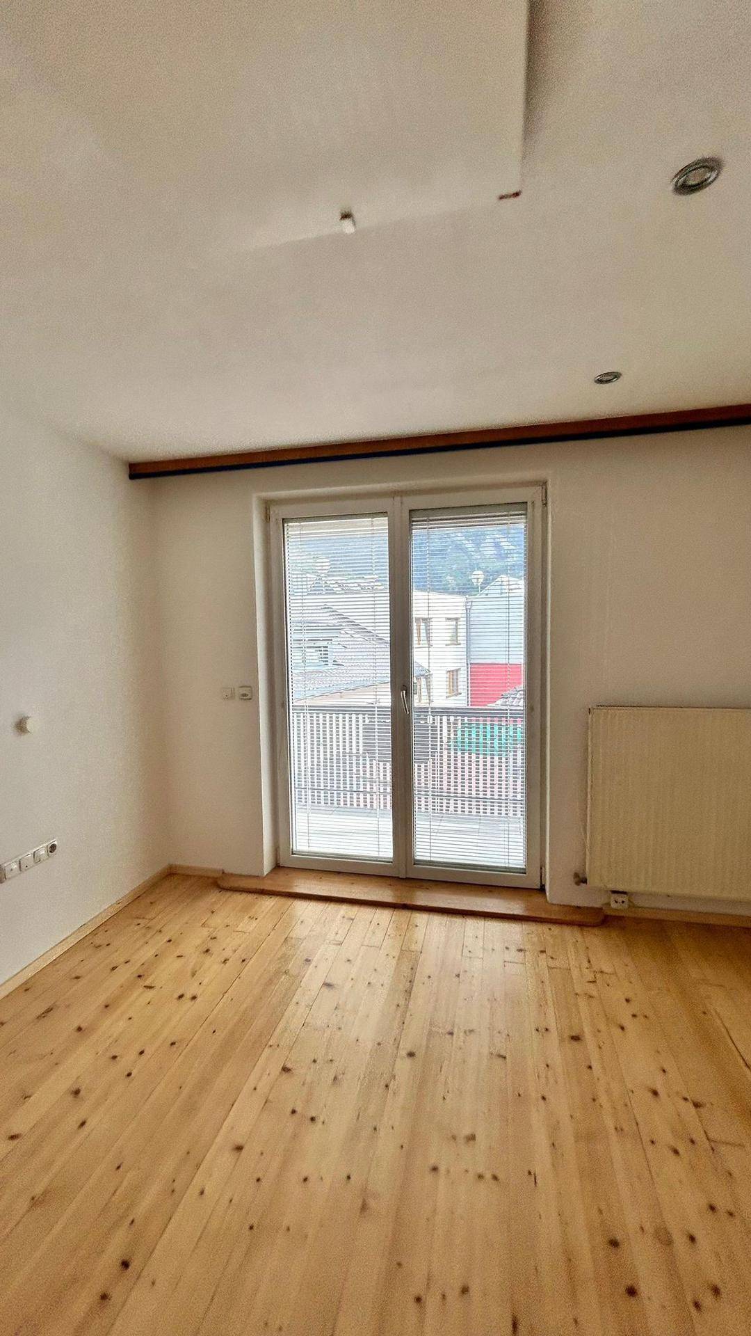 Helles Zimmer mit Holzdielenboden und Zugang zu einem Balkon, ideal als Schlaf- oder Wohnzimmer.
