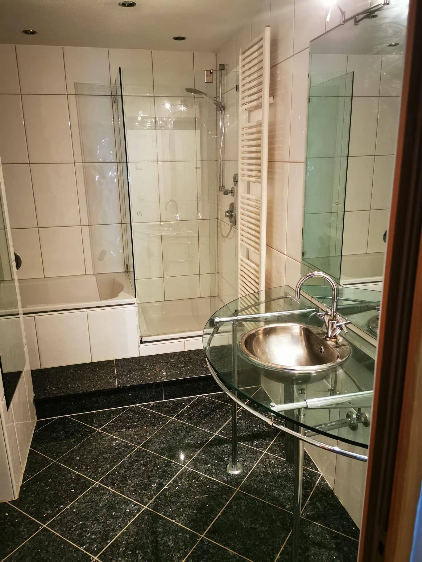 Modernes Badezimmer mit Duschkabine, Glaswaschtisch und dunklen Granitfliesen.