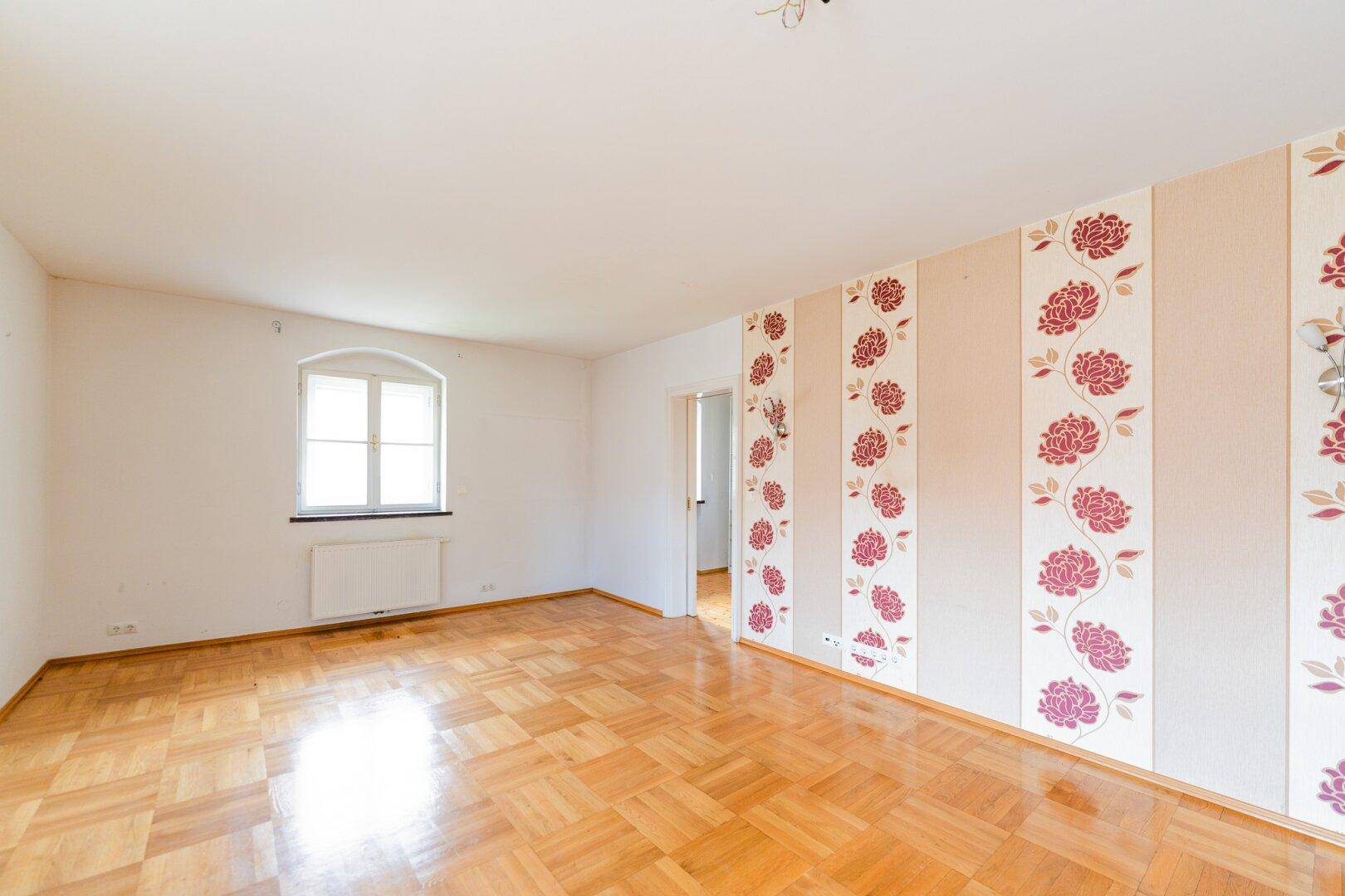 Helles Zimmer mit Parkettboden und einer Wand mit floraler Tapete, ideal für individuelle Gestaltung.