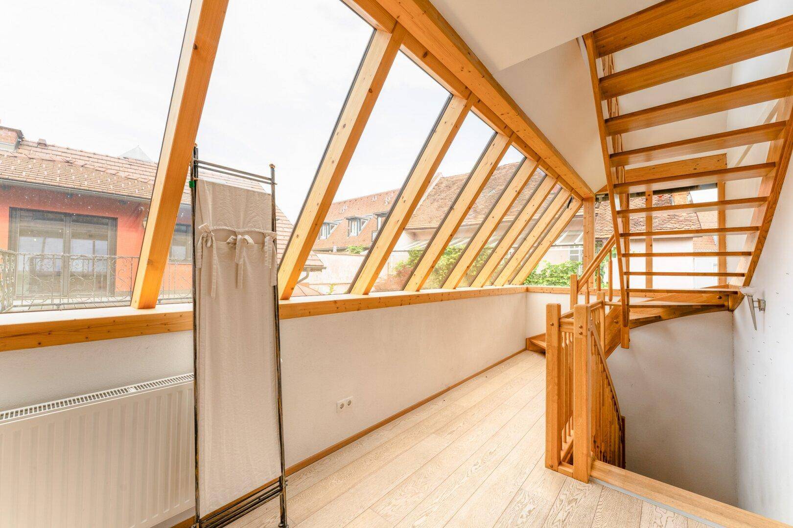 Heller Wintergarten mit Holztreppe und großen Dachfenstern, die viel Tageslicht hereinlassen.