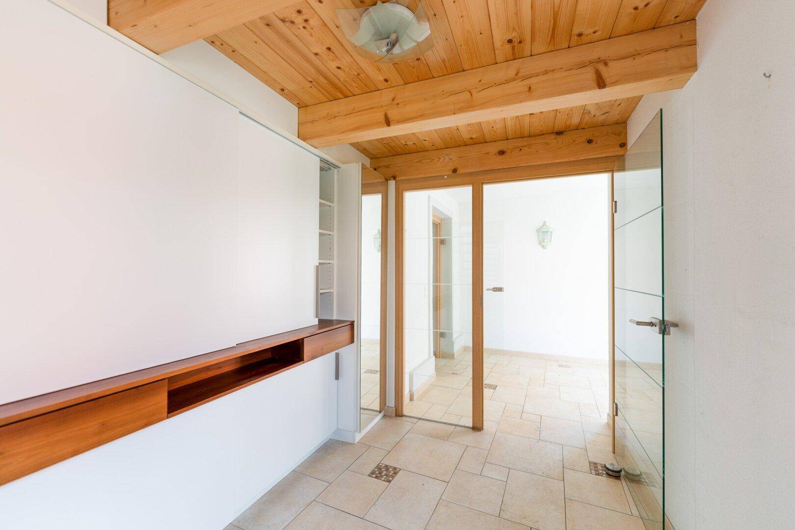Heller Eingangsbereich mit Holzdecke, Fliesenboden und integrierten Schränken.