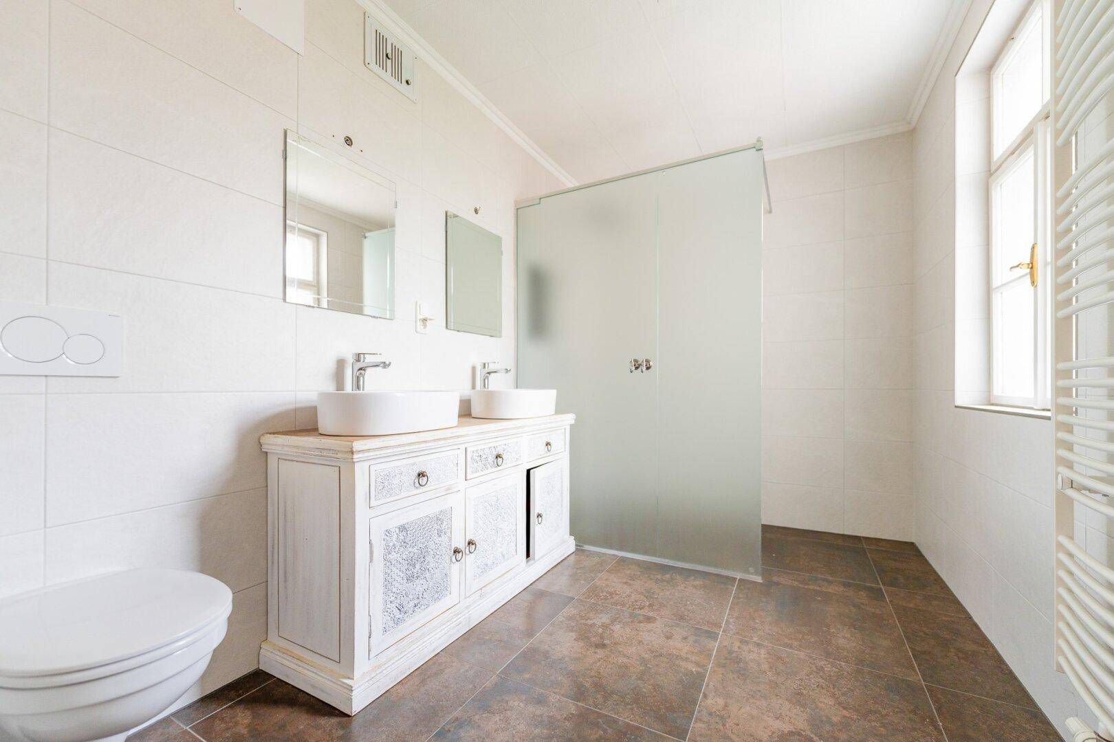 Helles Badezimmer mit Doppelwaschbecken, begehbarer Dusche und beheiztem Handtuchhalter.