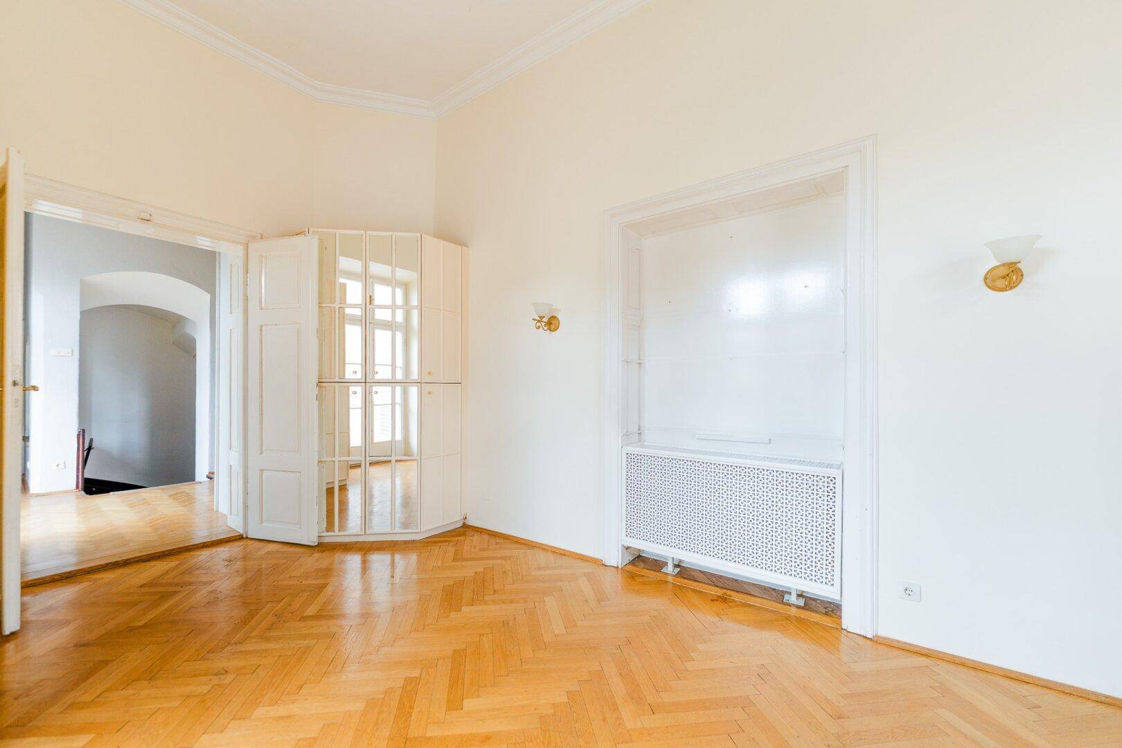 Geräumiges Zimmer mit Fischgrätparkett, Stuckdecken und einem dekorativen Heizkörper.