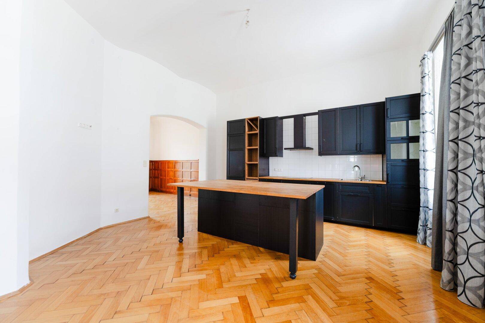 Offene Küche mit schwarzen Unterschränken, Holzinsel und Parkettboden, ideal für geselliges Kochen.