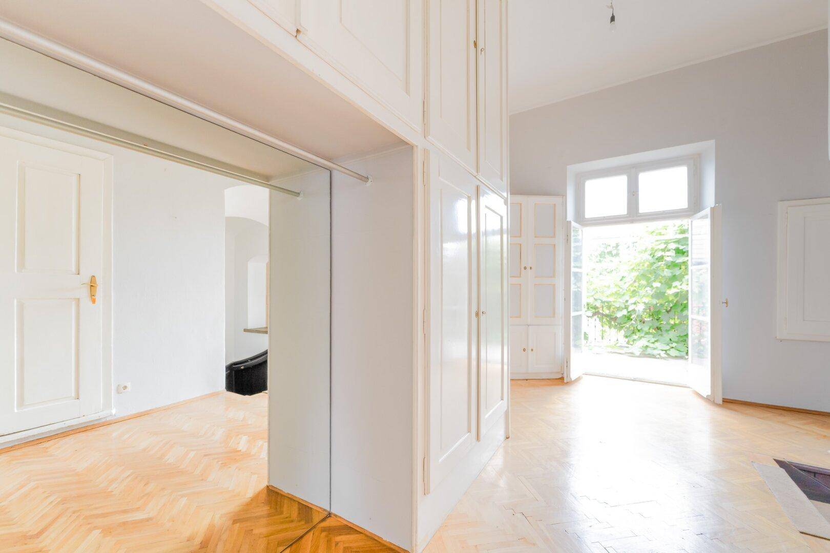 Helles Zimmer mit Parkettboden und integrierten weißen Schränken, mit Zugang zum Garten.