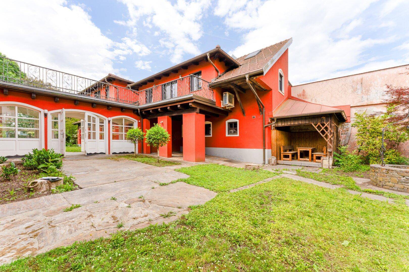 Rotes Haus mit großem Hof und überdachtem Sitzbereich im Freien unter hellem Himmel.