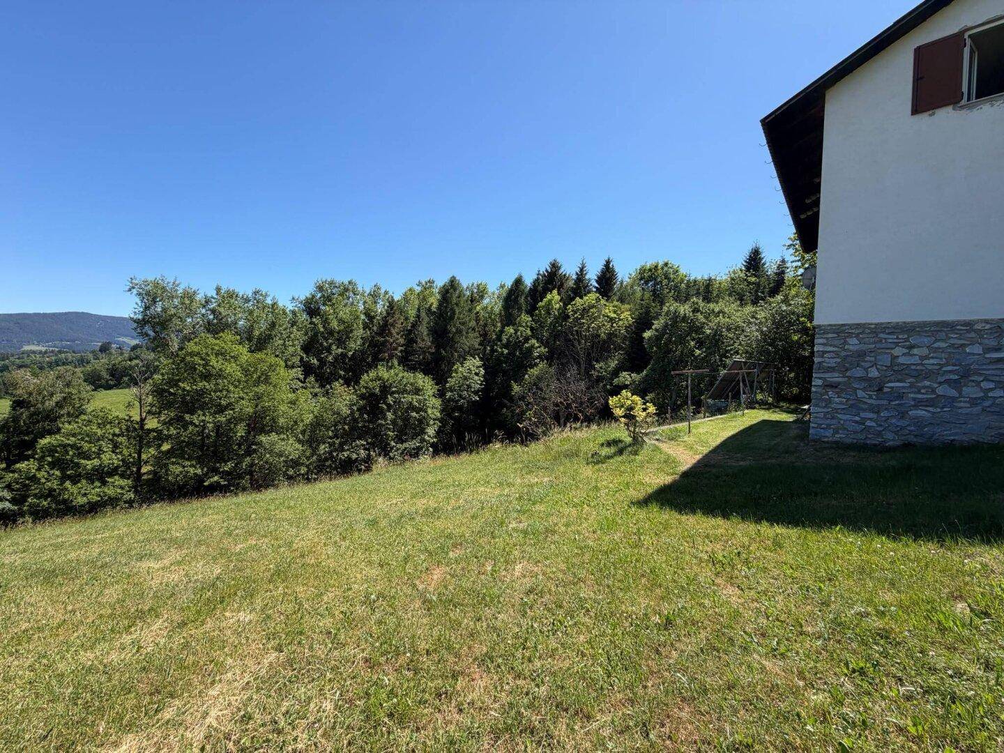 Hausfassade mit angrenzender Wiese und weitem Blick über die bewaldete Landschaft.