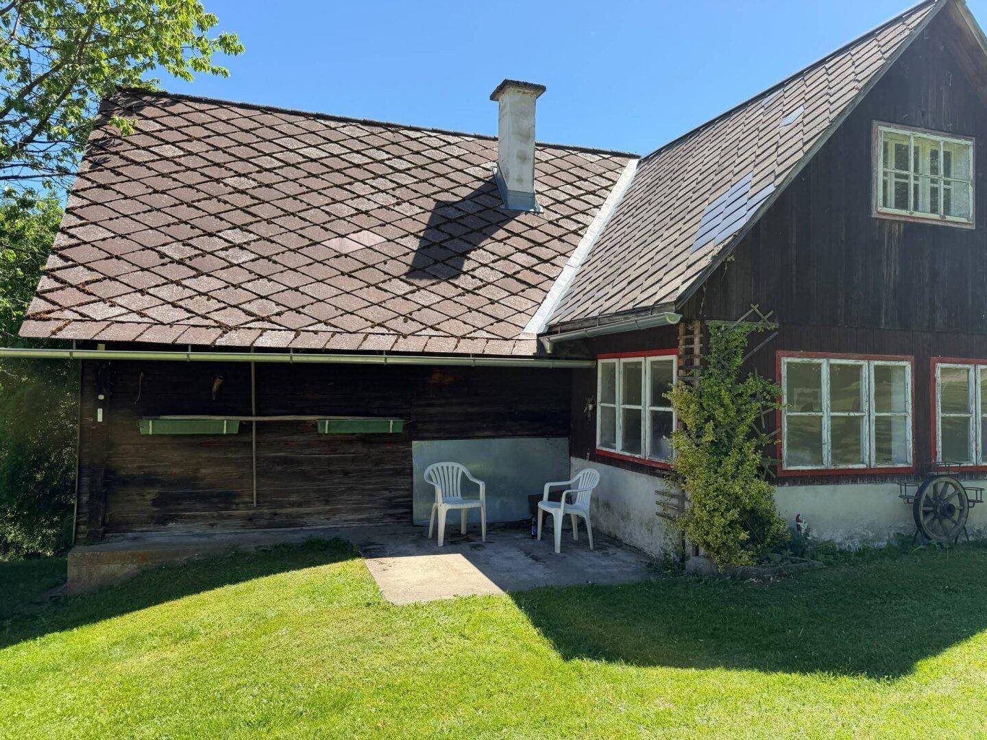 Rustikales Haus mit kleiner Terrasse und Gartenmöbeln auf der Rasenfläche.
