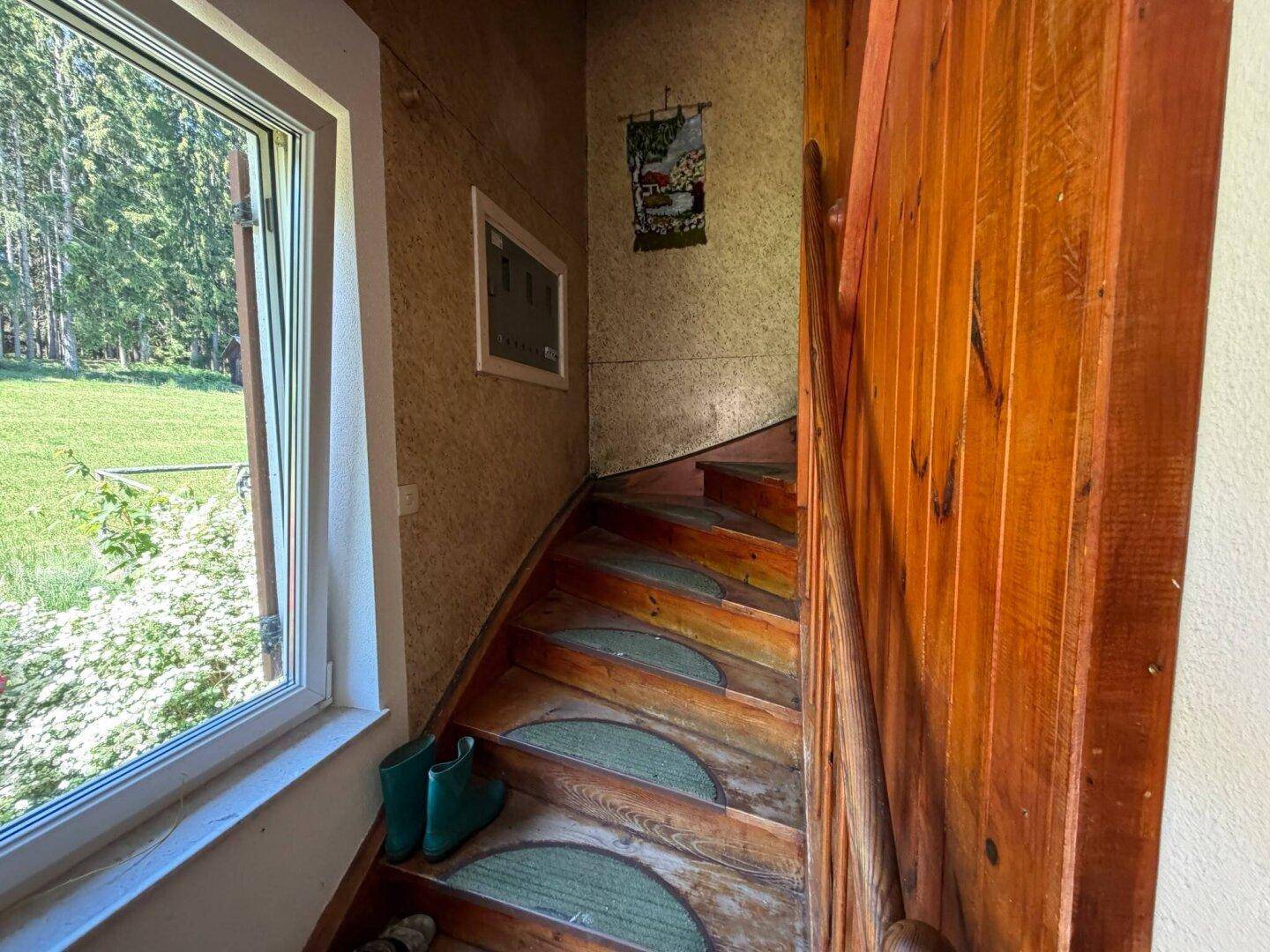 Rustikale Holztreppe mit Teppichstufen und Fensterblick ins Grüne.