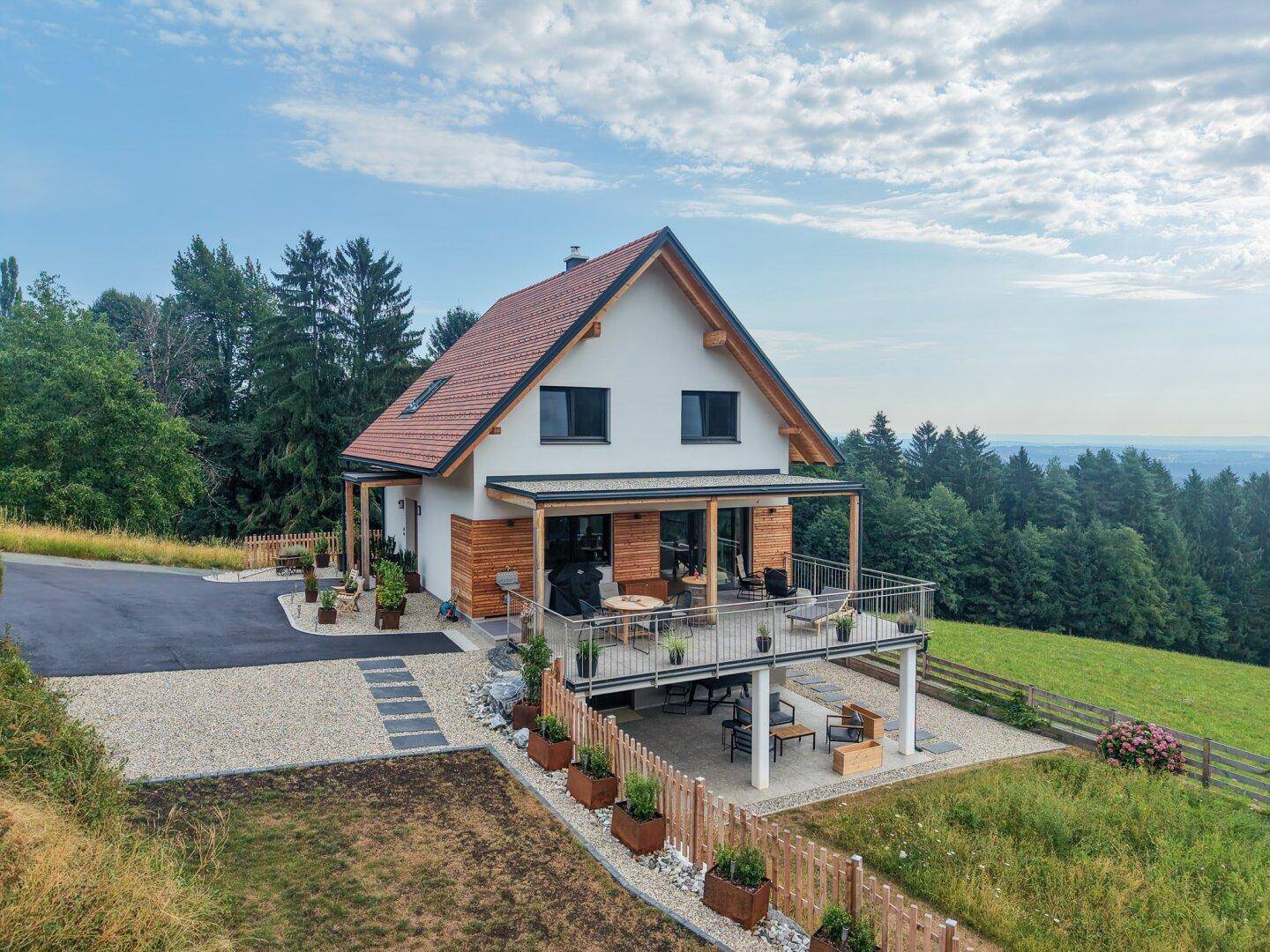Freistehendes Haus mit großer Terrasse und überdachtem Bereich, umgeben von grüner Natur.