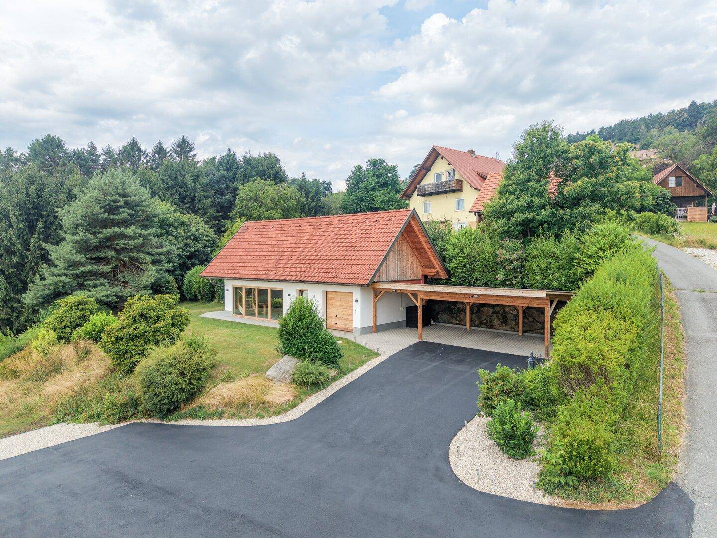 Modernes Haus mit Carport und gepflegtem Garten, umgeben von viel Grün.