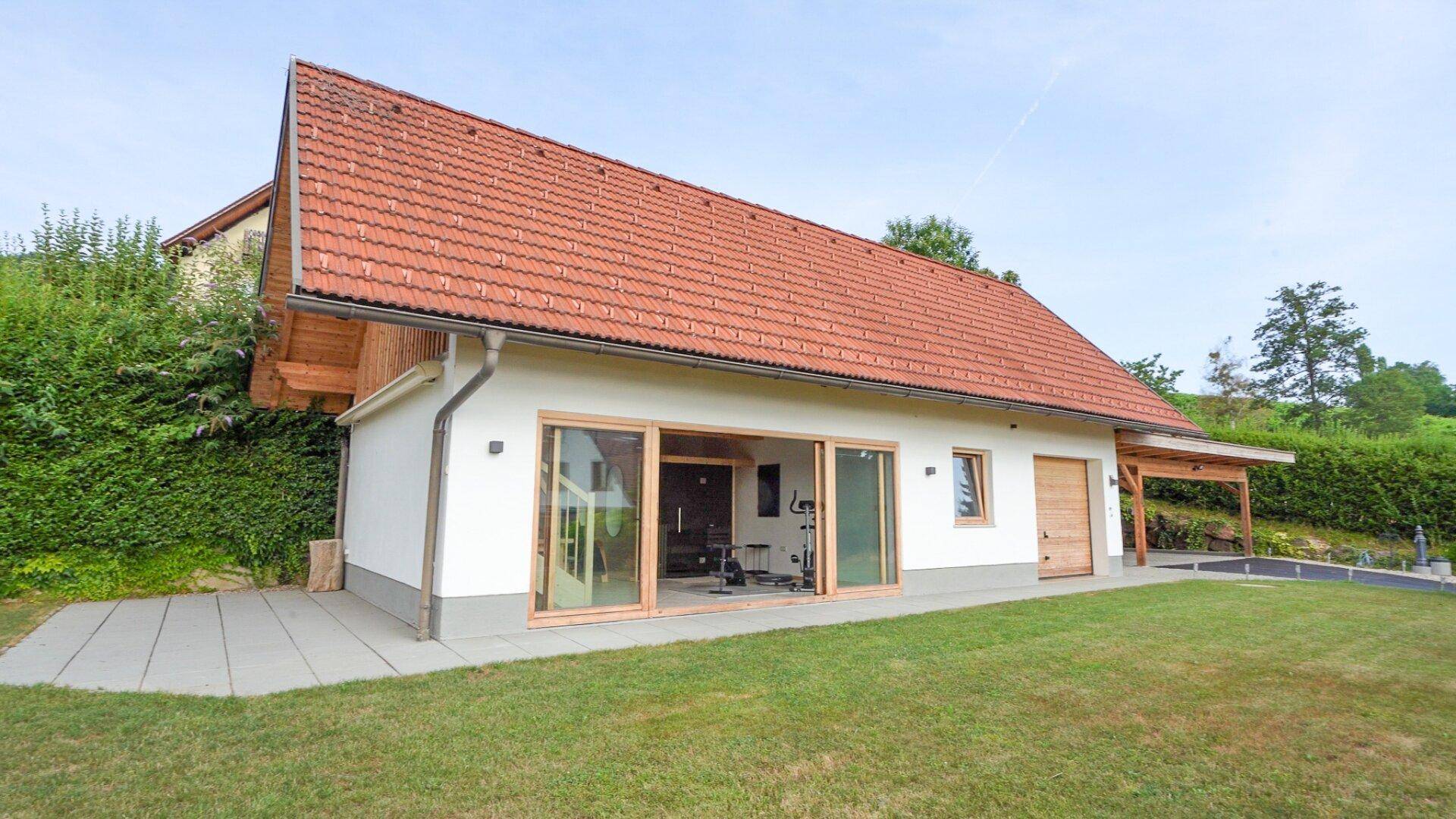 Rückseite des Hauses mit großen Glasfronten, Zugang zum Garten und Carport.