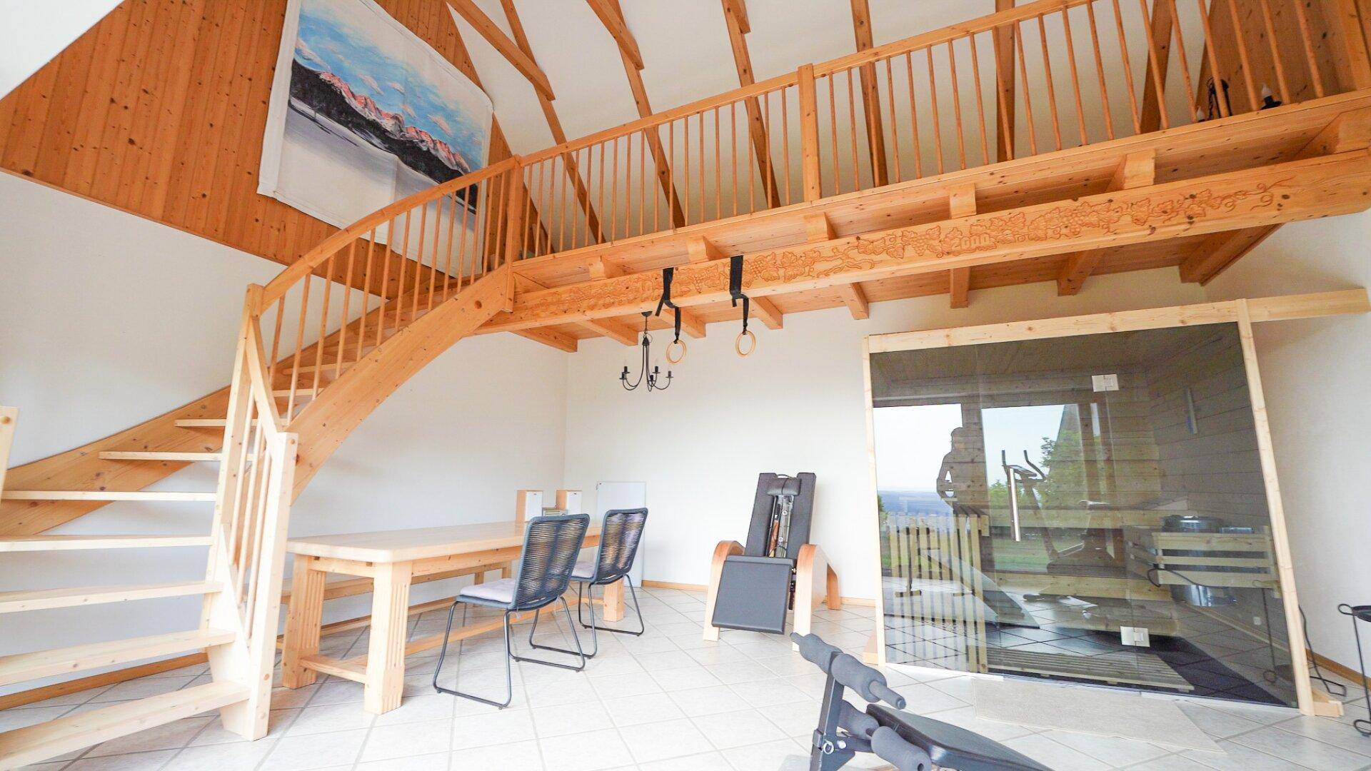 Fitnessraum mit Sauna, Trainingsgeräten und Holztreppe zu einer Galerie.