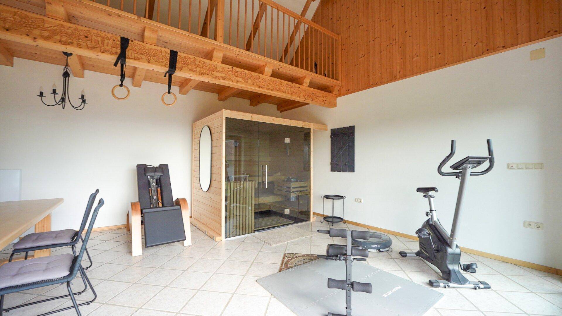 Heller Fitnessbereich mit Sauna, verschiedenen Sportgeräten und Holzelementen.