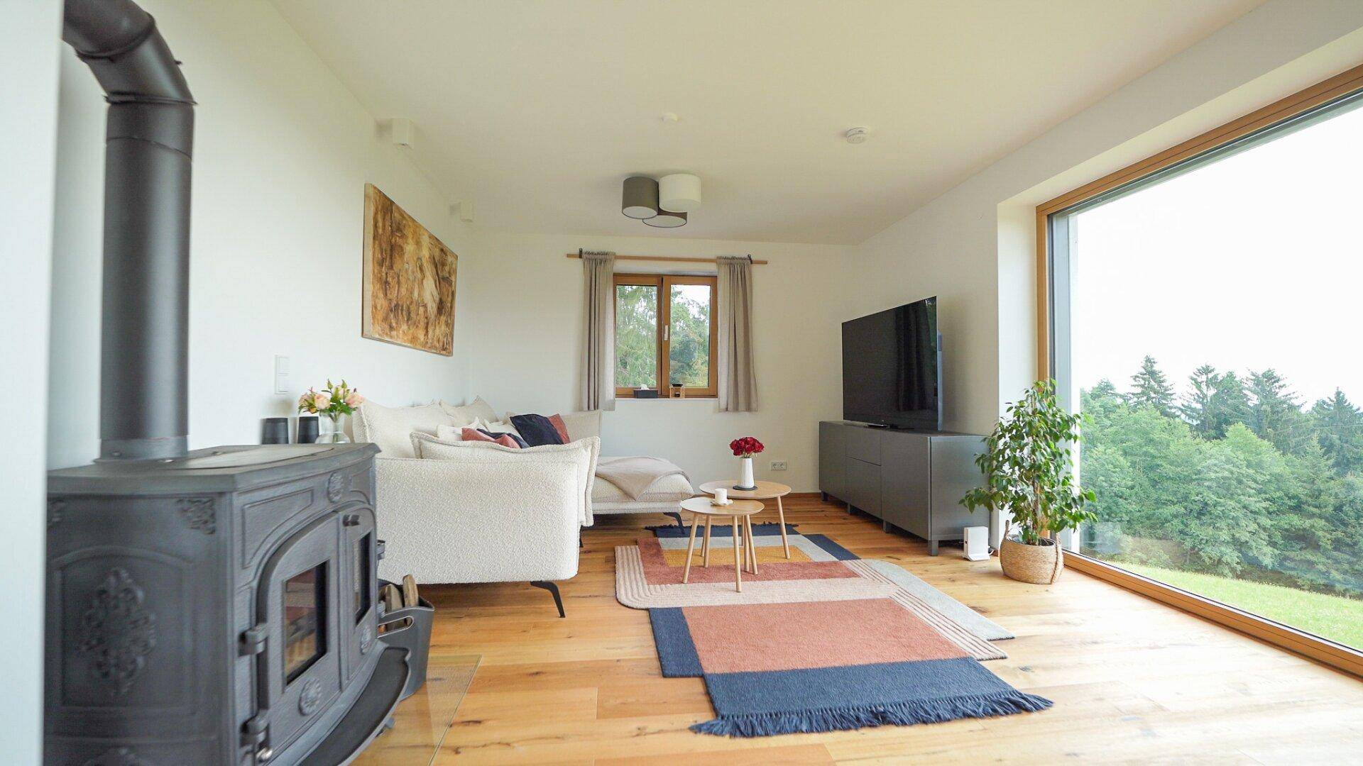 Gemütliches Wohnzimmer mit Kaminofen, Holzboden und großem Fenster mit Weitblick.
