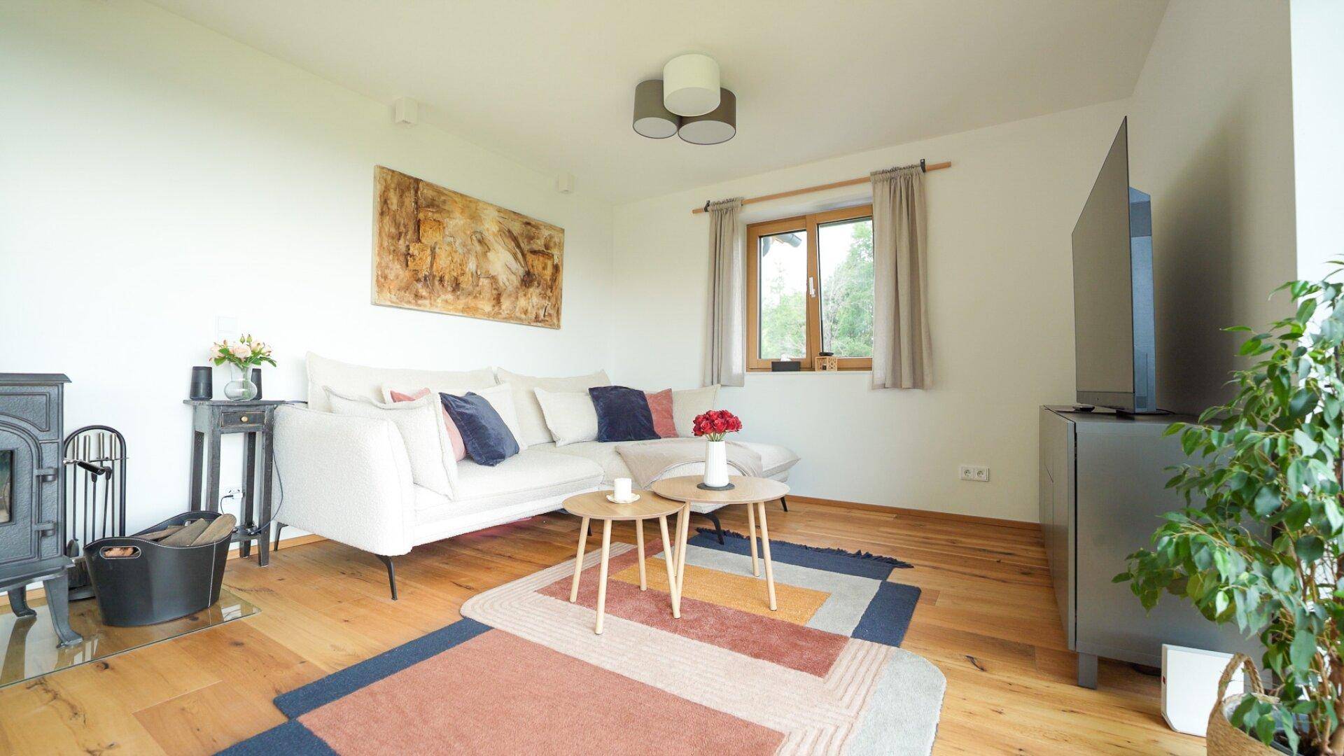 Helles Wohnzimmer mit bequemer Couch, Kaminofen und Blick auf die grüne Umgebung.