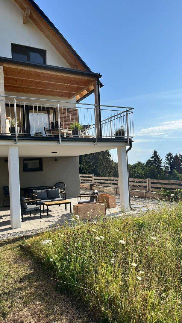 Modernes Haus mit Balkon, überdachter Terrasse und weitläufigem Gartenbereich.