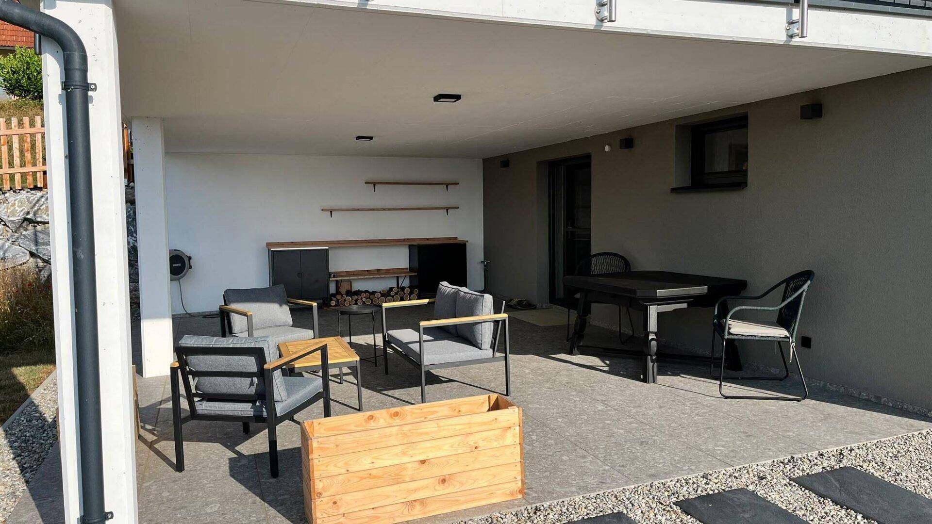 Überdachte Terrasse mit Sitzgelegenheiten, Außenküche und Blick in den Garten.