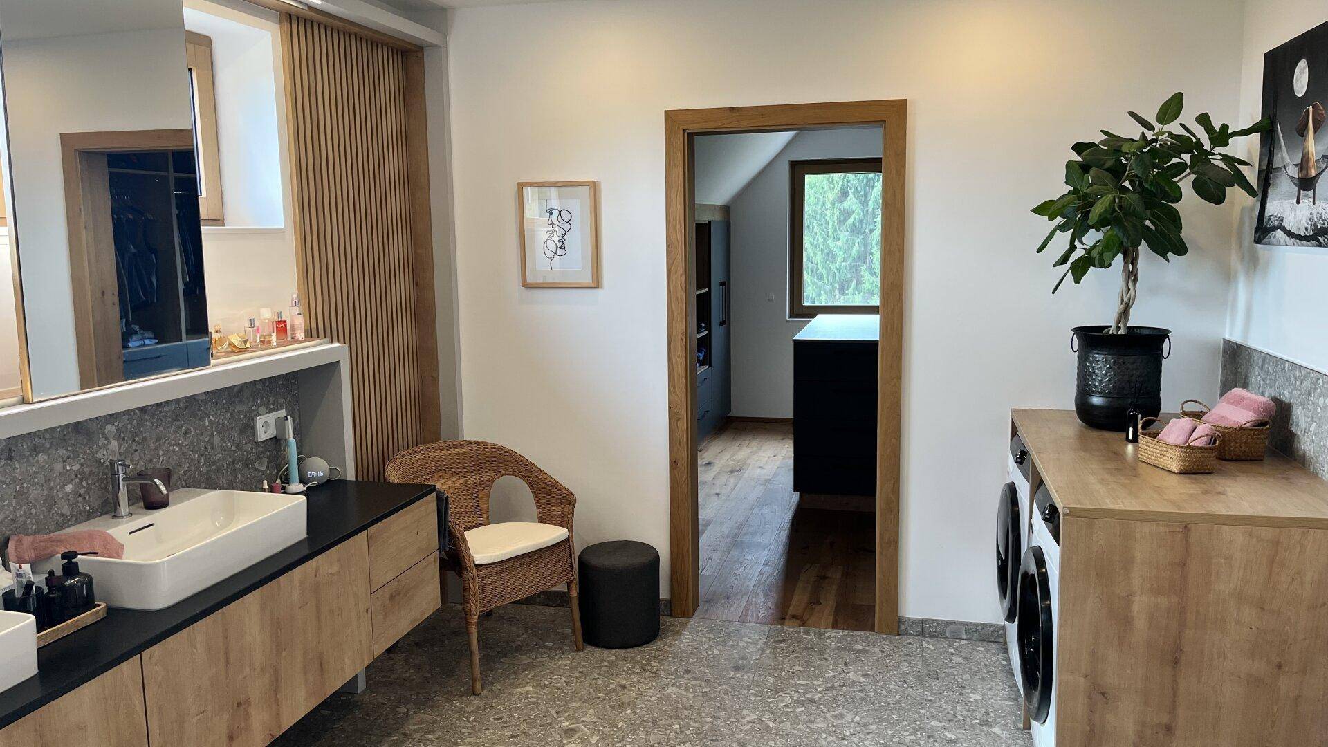 Geräumiges Badezimmer mit Doppelwaschbecken, Waschmaschine und Zugang zu einem Ankleidezimmer.