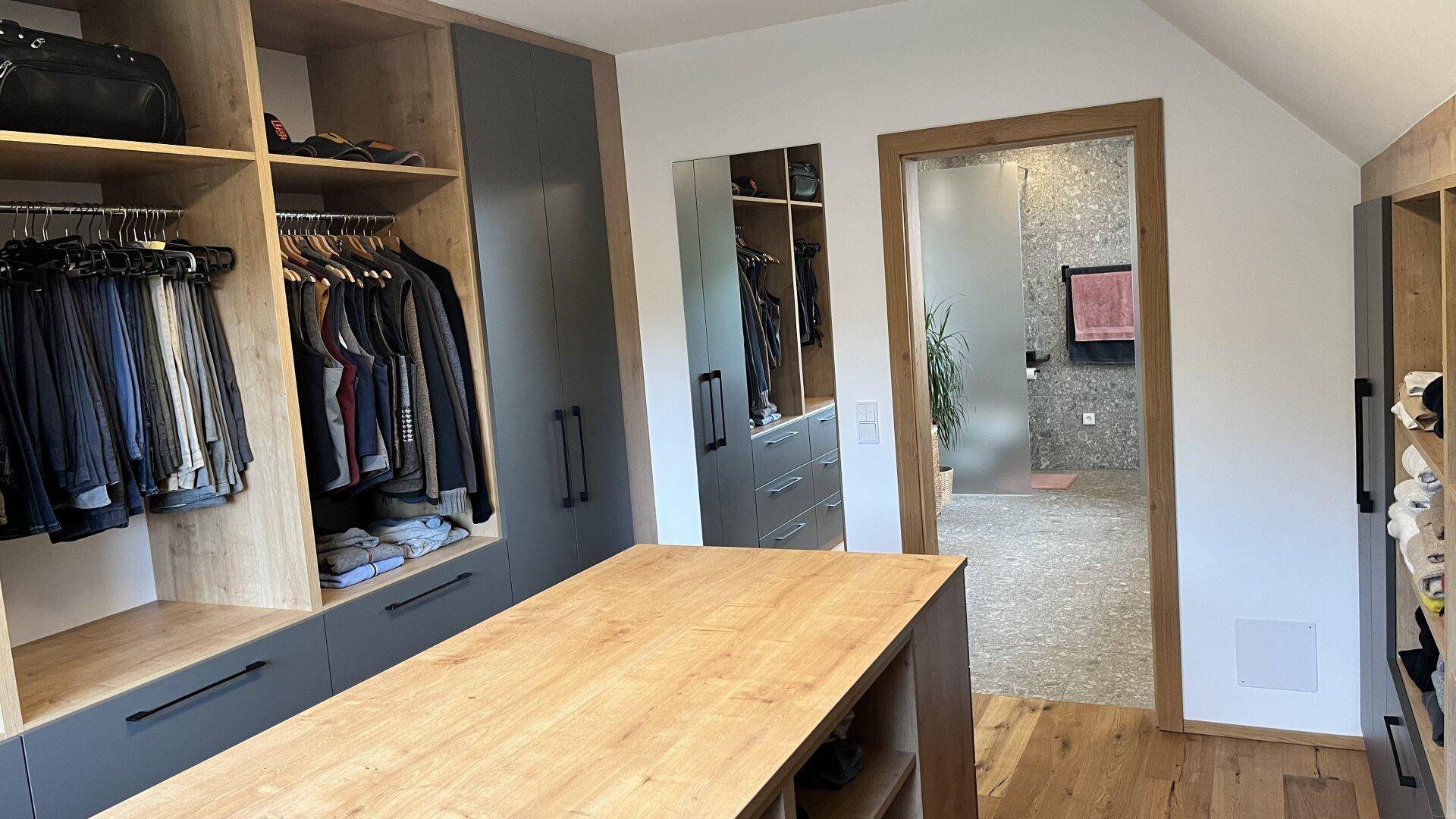 Ankleidezimmer mit Holzboden, Einbauschränken und direktem Zugang zum modernen Badezimmer.