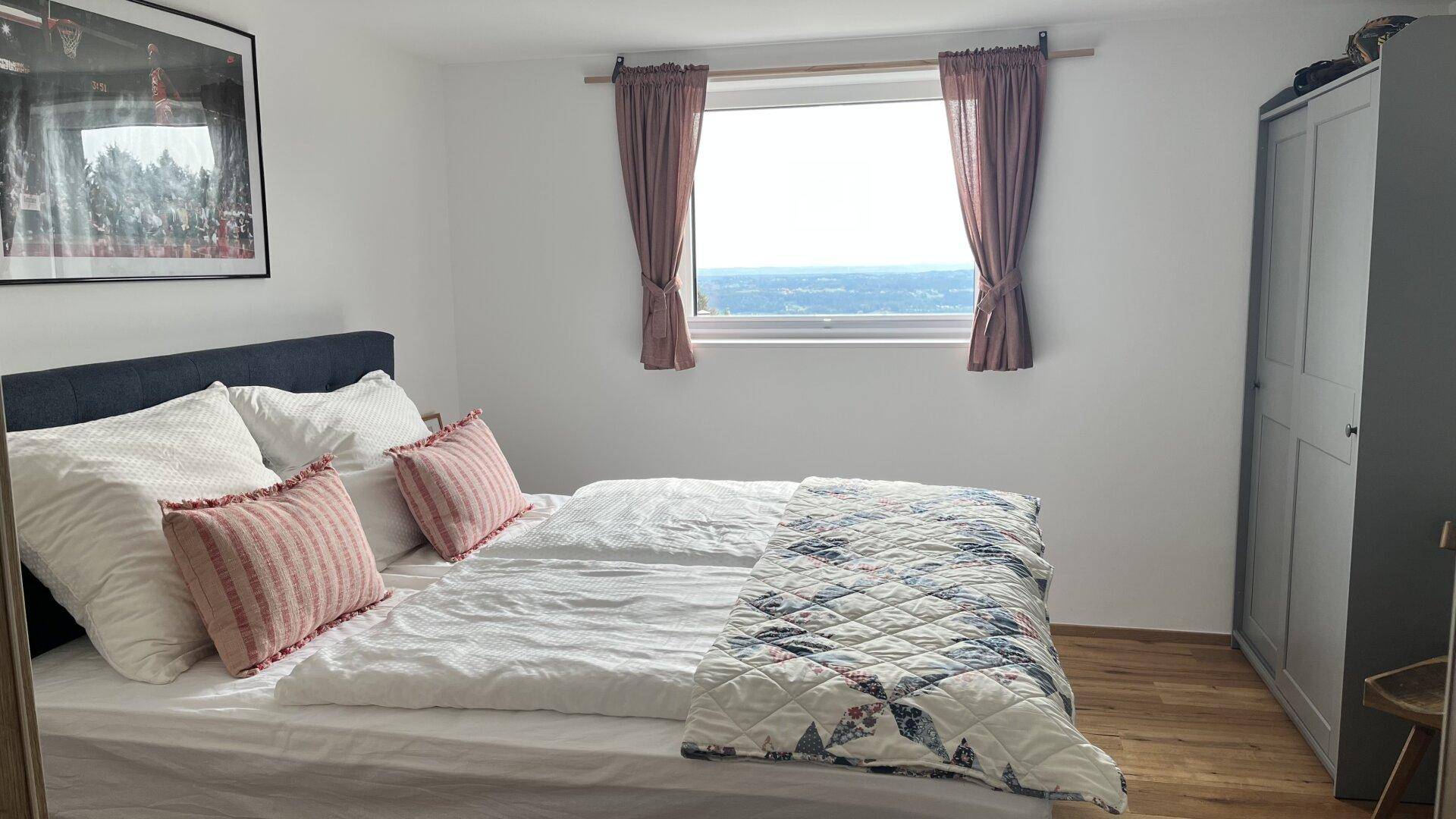 Helles Schlafzimmer mit Doppelbett, Holzboden und weitem Blick aus dem Fenster.