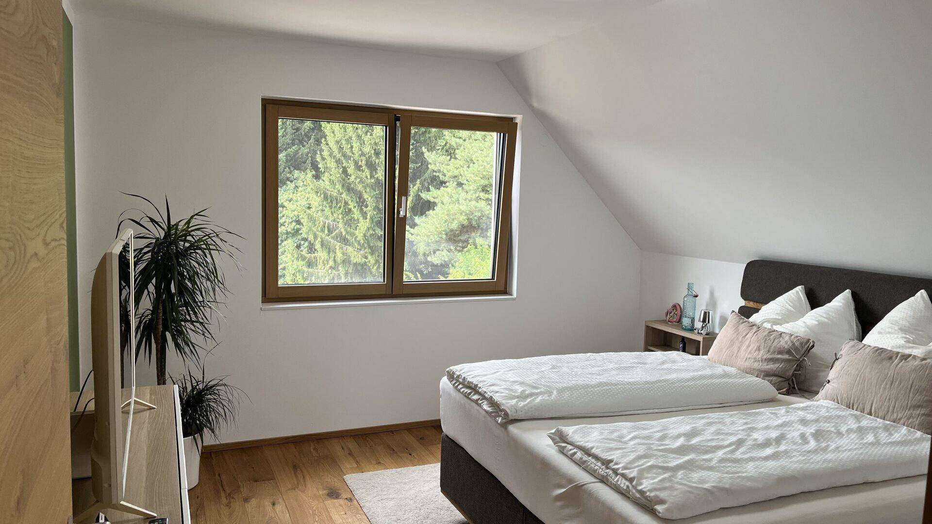 Gemütliches Schlafzimmer mit Holzboden, Dachschräge und Blick ins Grüne durch das Fenster.