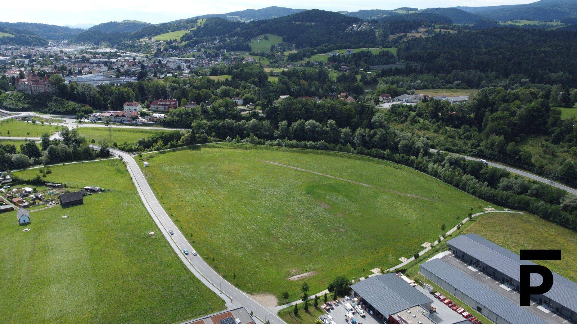 Panoramablick auf ein großes grünes Feld mit umliegender Landschaft, Stadt und Bergen im Hintergrund.