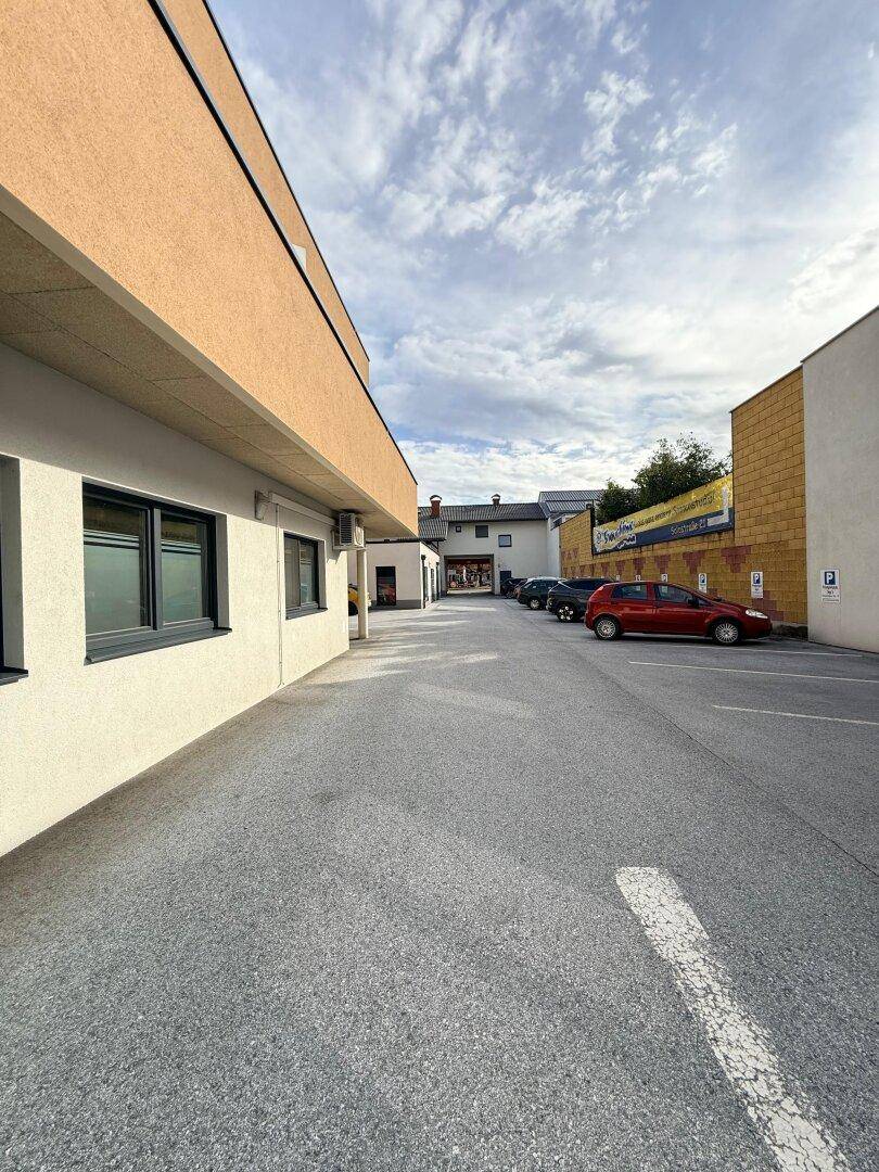 Seitenansicht des Gebäudes entlang eines Parkplatzes mit weiteren Gebäuden in der Ferne.