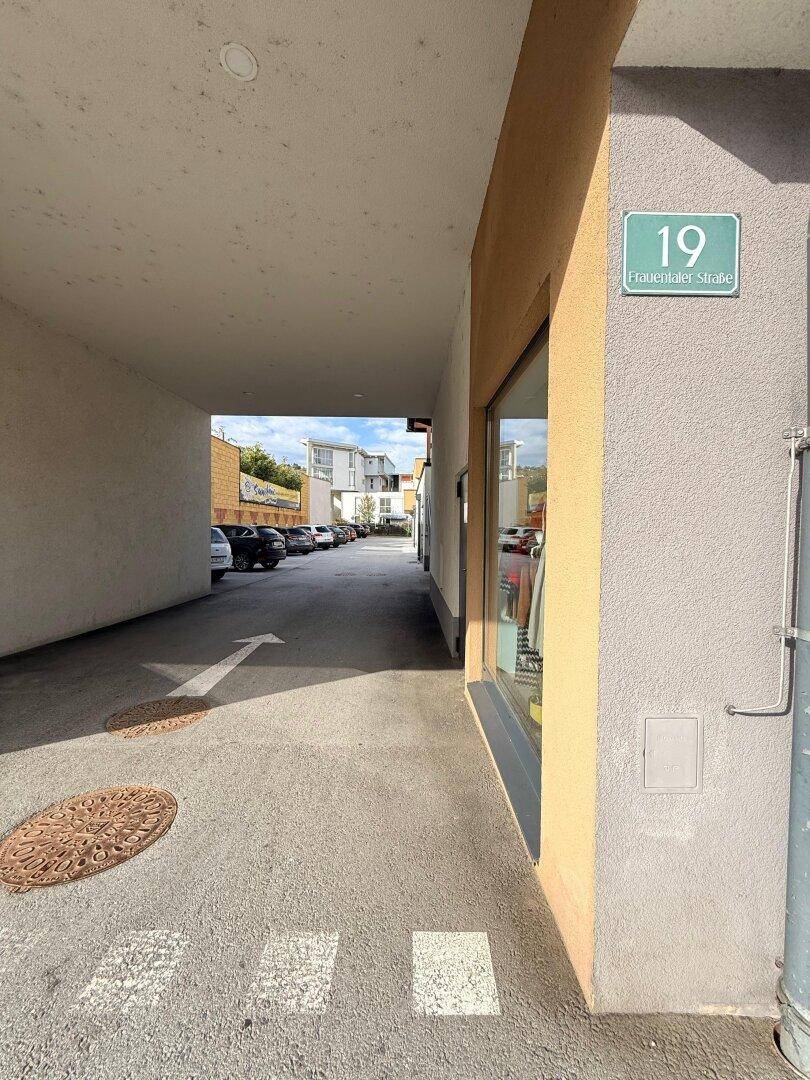 Überdachter Durchgang zu einem Parkplatz mit einem Straßenschild "Frauenthaler Straße 19".