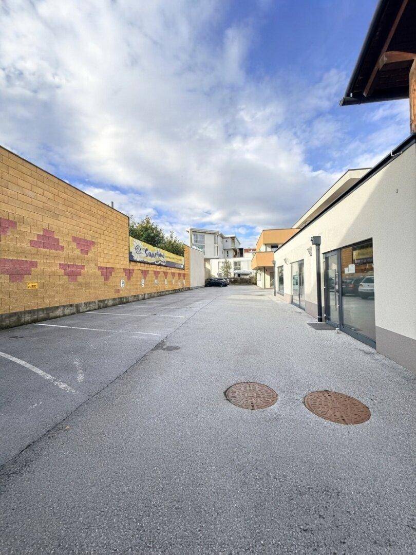 Langer Parkplatz zwischen Gebäuden mit einer gelb-roten Ziegelwand auf der linken Seite.