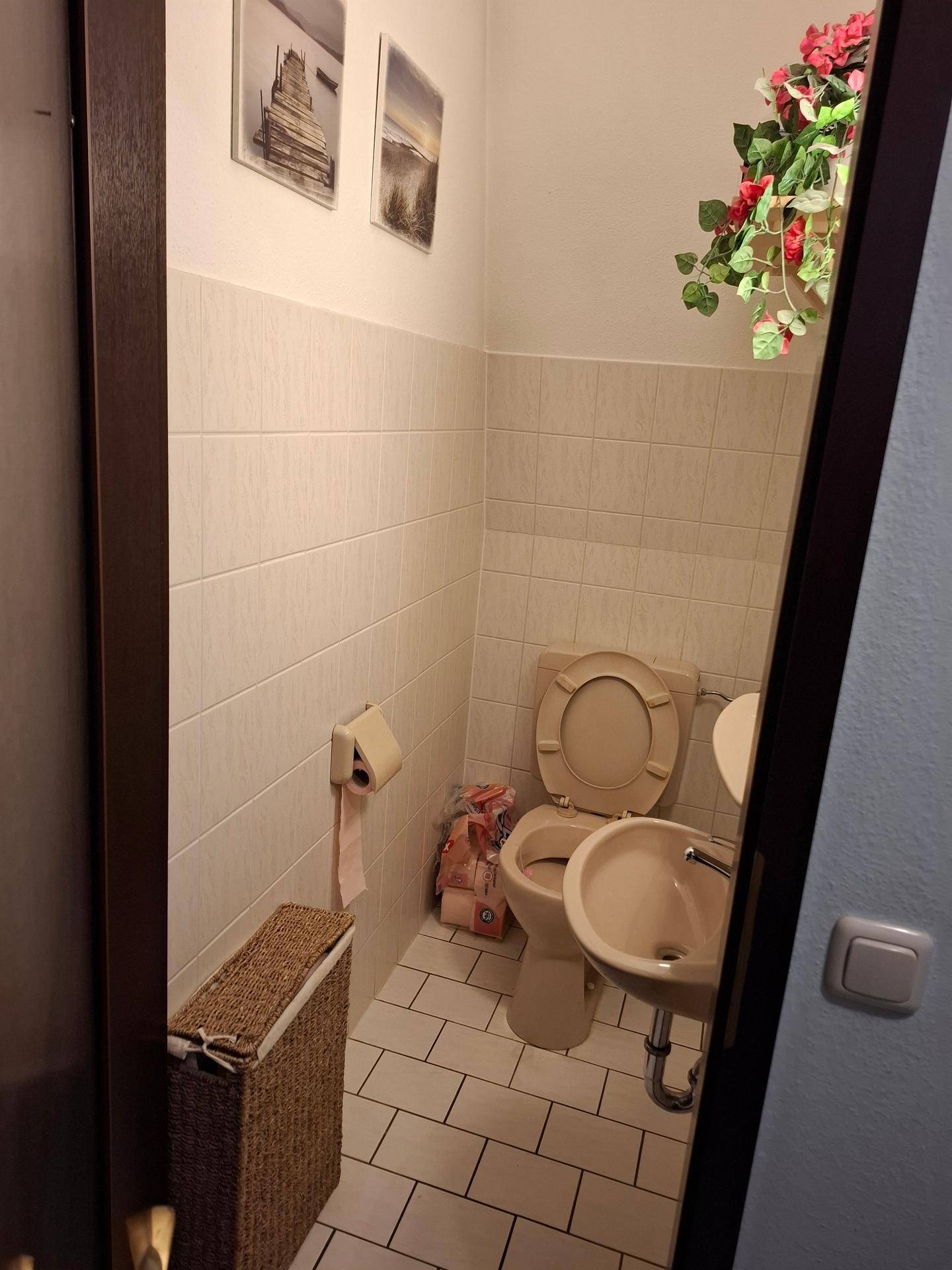 Kleines Gäste-WC mit beigefarbenen Fliesen, Toilette und einem kleinen Waschbecken.