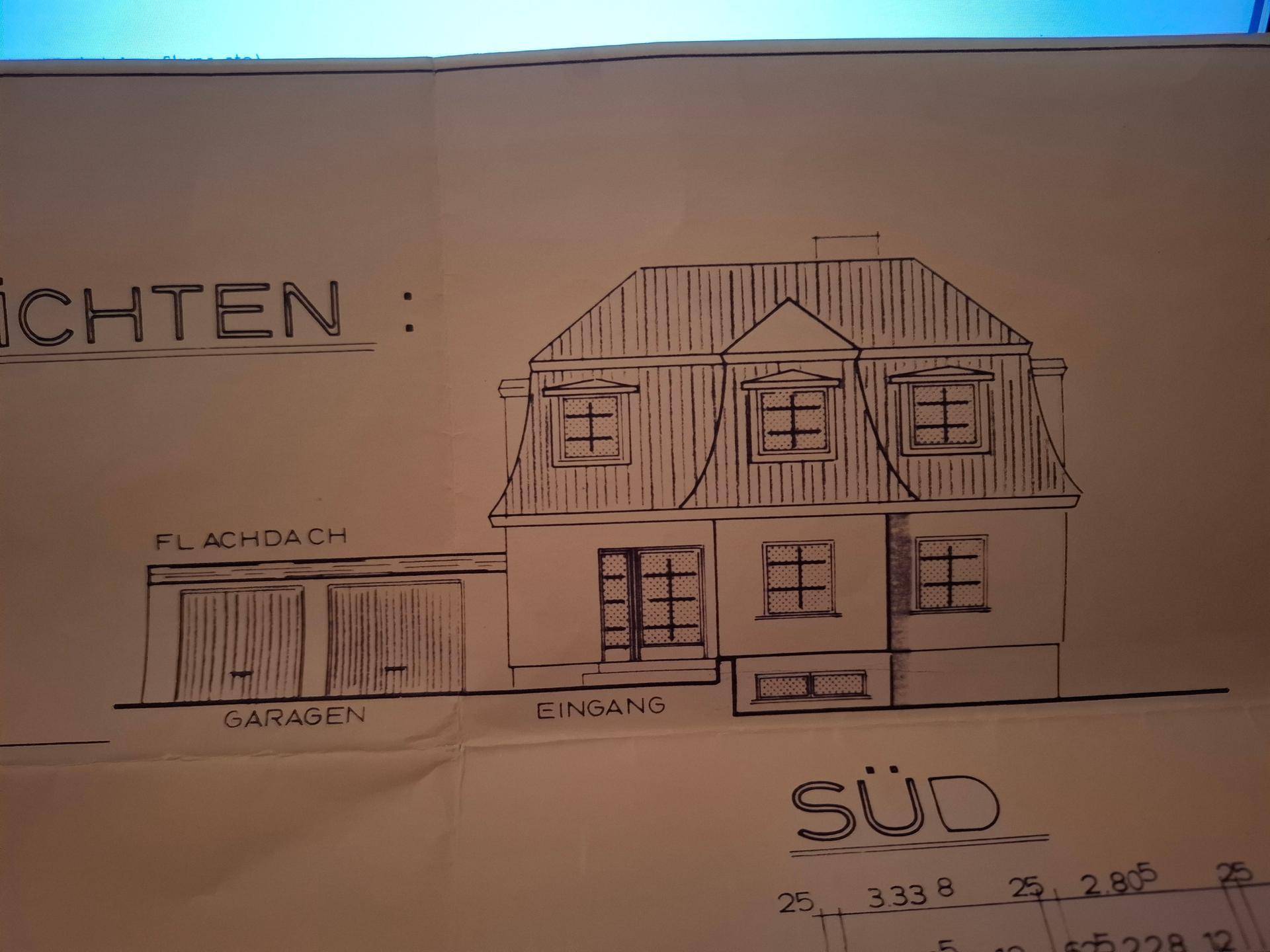 Südansicht des Hauses mit Mansarddach und integrierten Garagen.