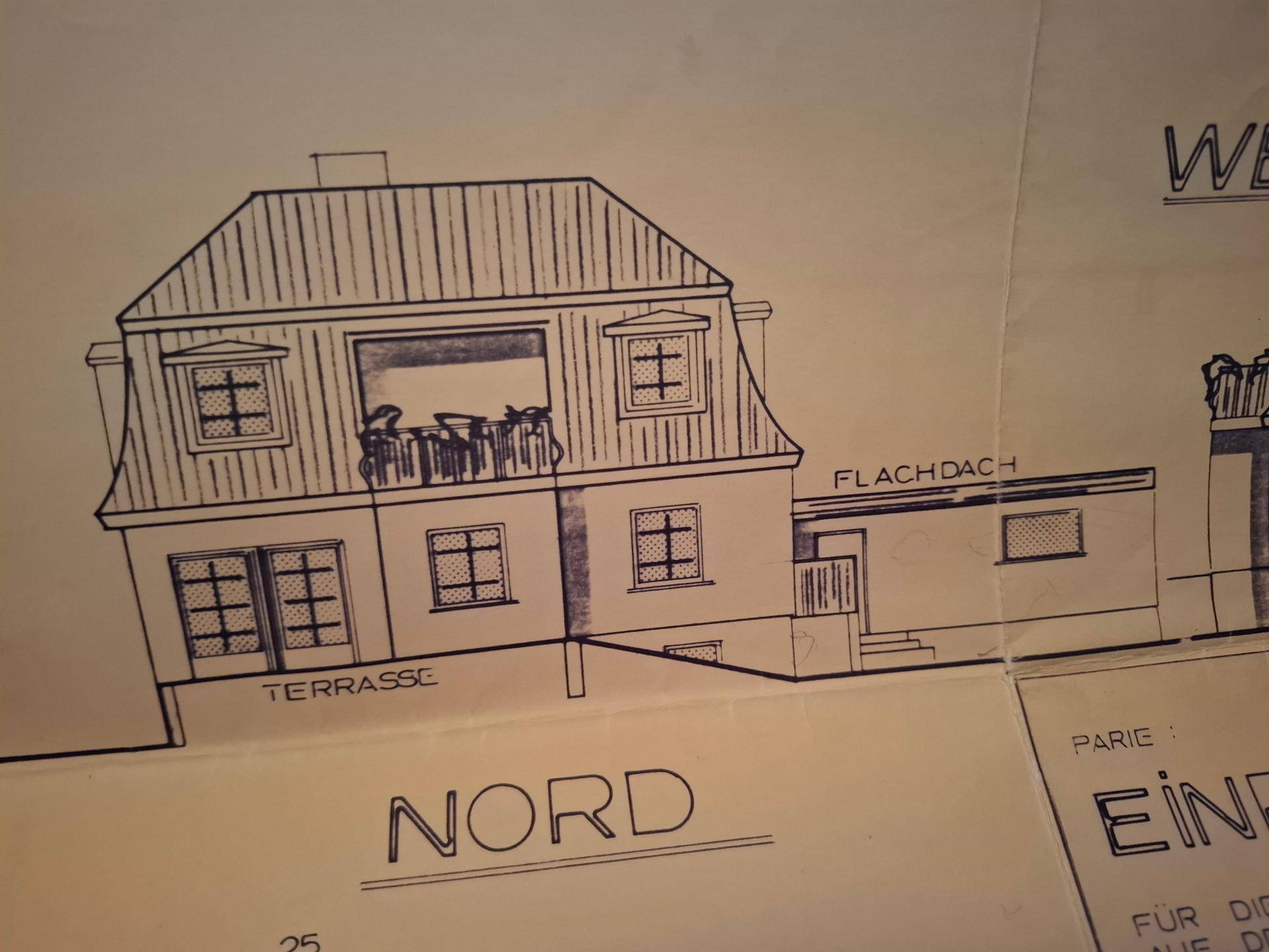 Nordansicht des Hauses mit Mansarddach, Terrasse und Balkon im Obergeschoss.