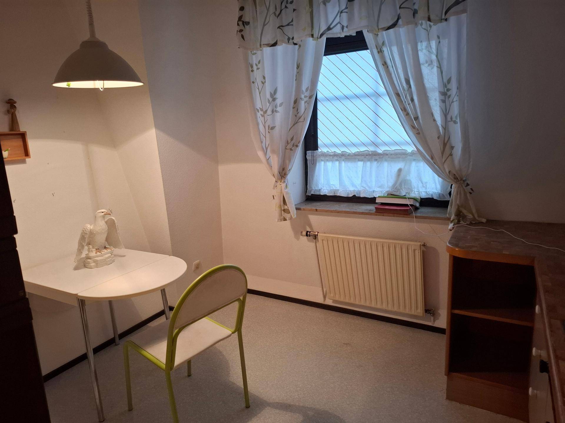 Kleiner Raum mit Schreibtisch, Stuhl und Fenster, ideal als Büro oder Gästezimmer.