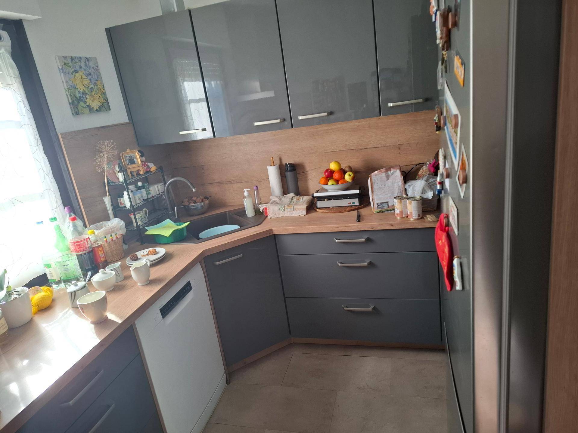 Moderne Küche mit grauen Hochglanzschränken, Holzarbeitsplatten und integriertem Geschirrspüler.